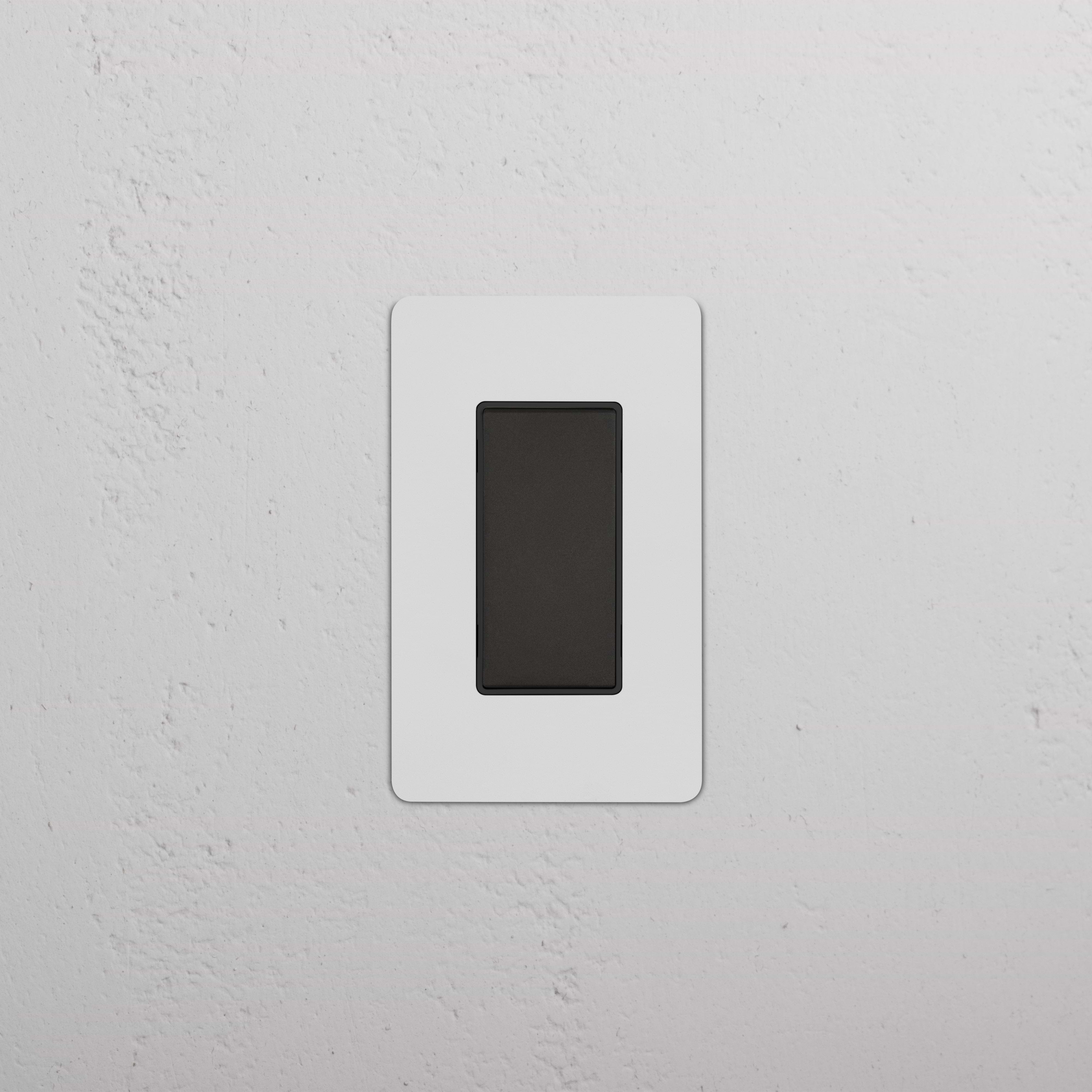 Kew 1G Center Retractive Rocker Switch in paintable bronze black finish, installed on a white wall.