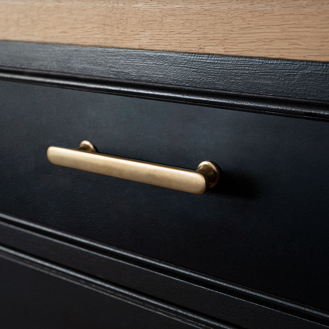 Close-up of a Milliner Furniture Handle Small in antique brass mounted on a dark drawer.