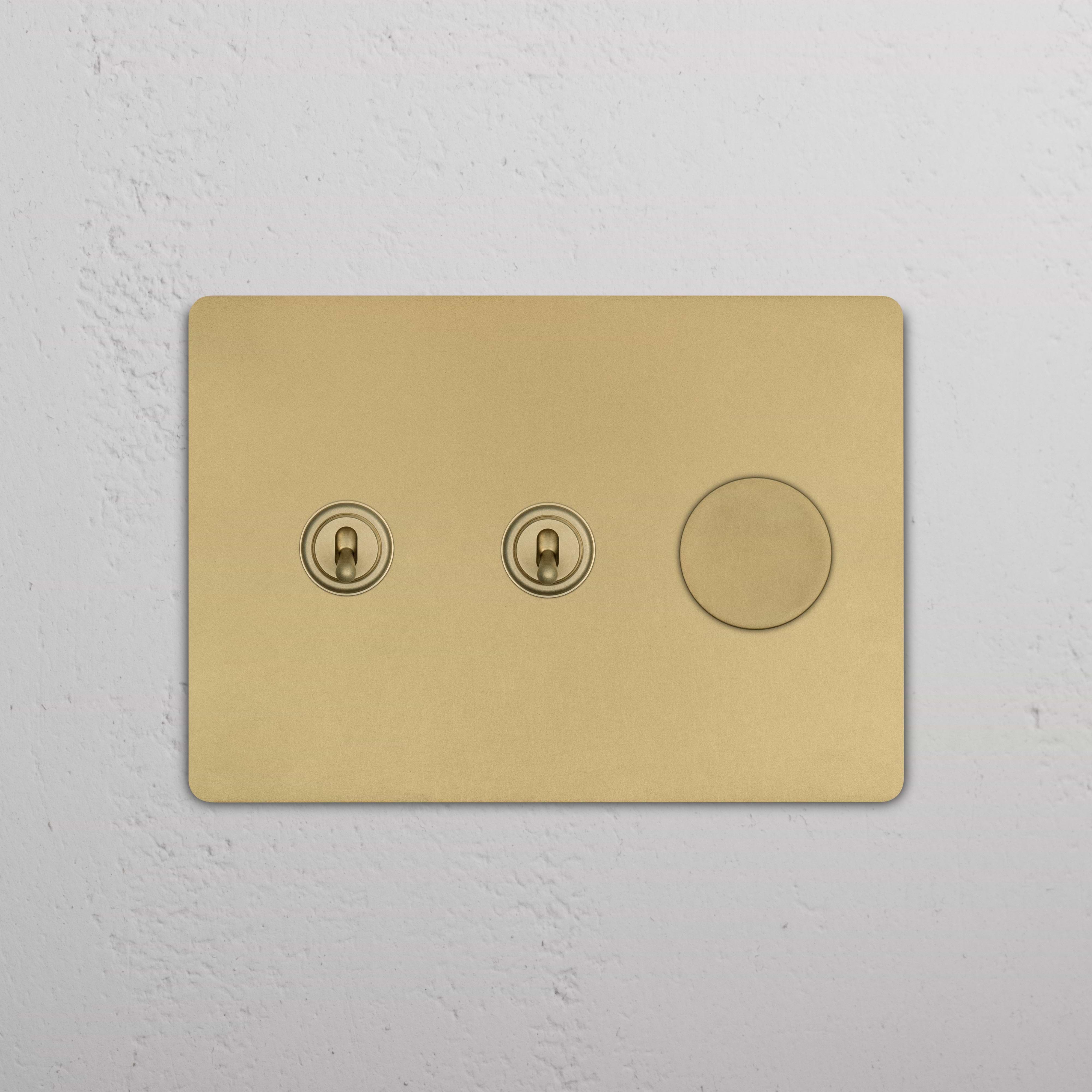 Grove 3G antique brass switch with two toggles and one dimmer, mounted on a textured white wall.