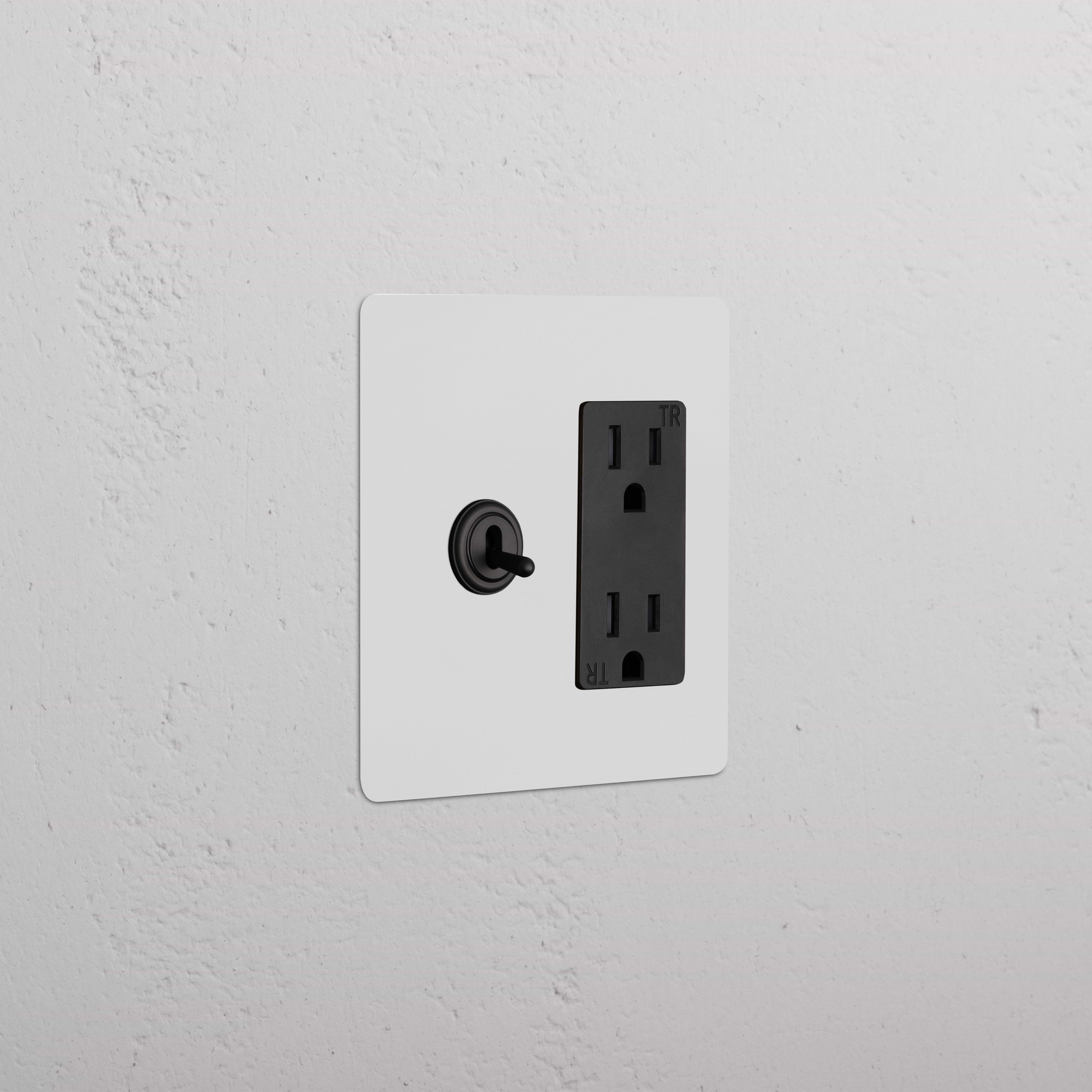 Kew 2G Toggle Switch & Outlet in Paintable Bronze Black on a white wall plate, mounted on a white wall.