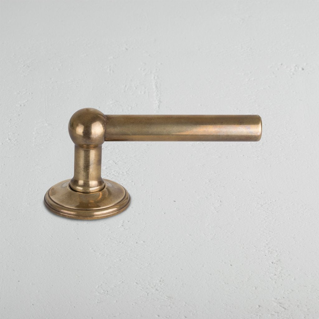 Harper Dummy Door Handle Set in antique brass with cylindrical lever and round base on light gray surface.