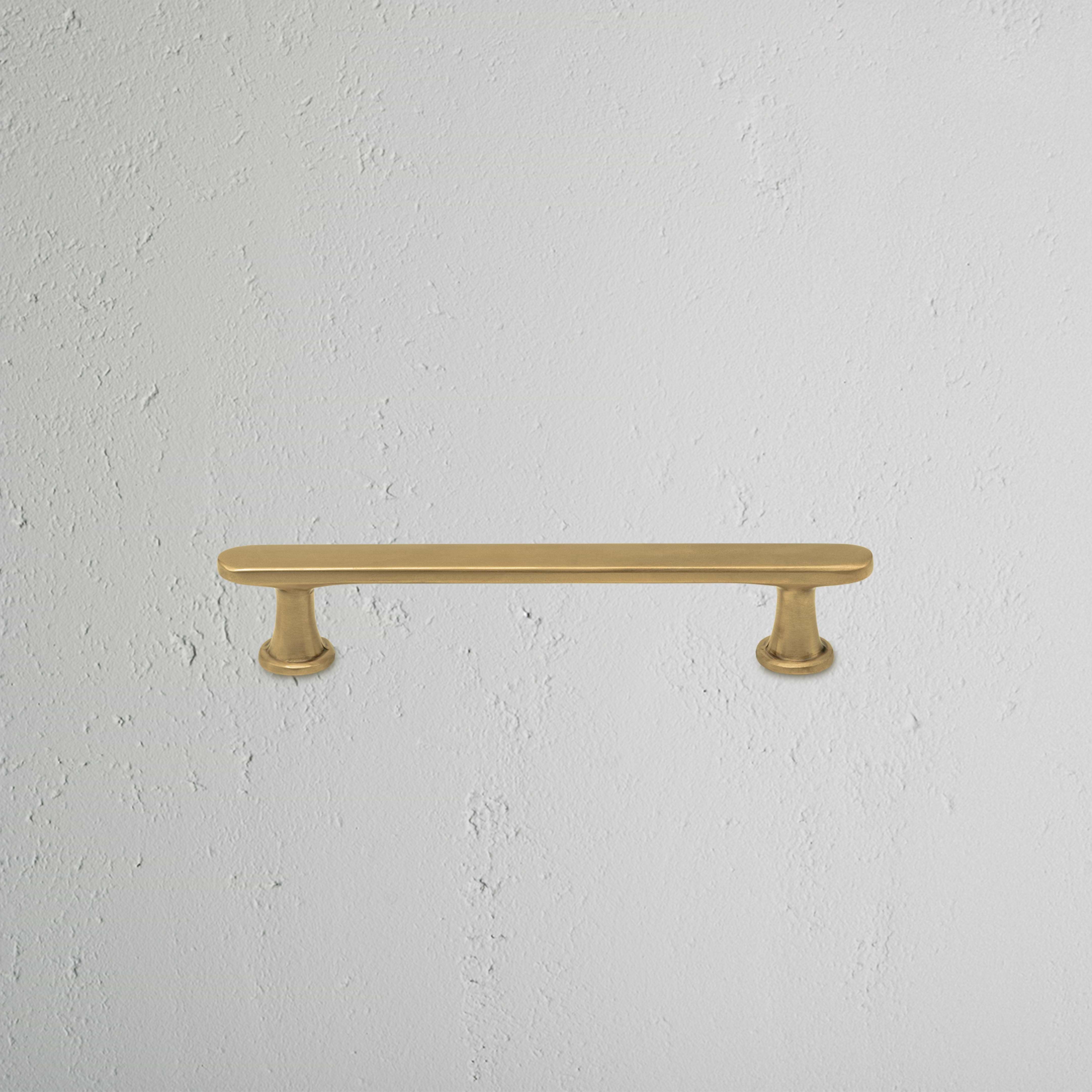 Milliner Furniture Handle Small in antique brass with rounded ends, mounted on a white textured wall.