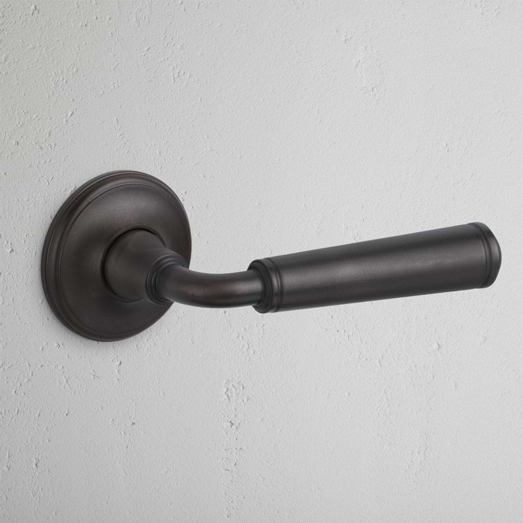 Bronze Digby Passage Door Handle Unsprung with a round base plate, mounted on a light wall.