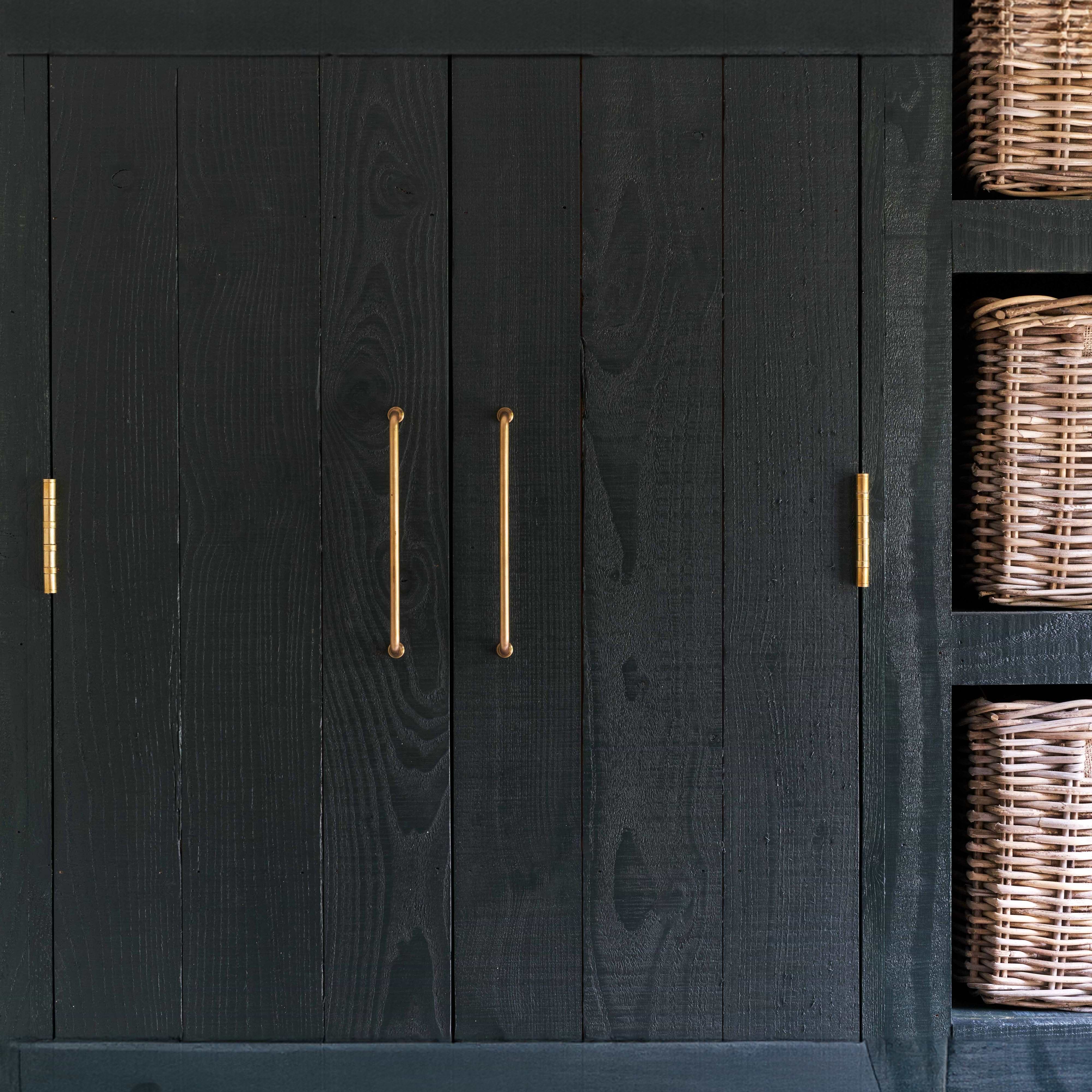 Medium Sycamore Furniture Handle in antique brass finish, mounted on a wooden cabinet door.