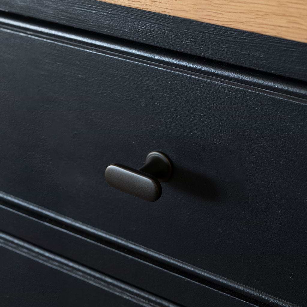 Close-up of a bronze Milliner Furniture Knob on a black drawer, with a light wood top edge visible.