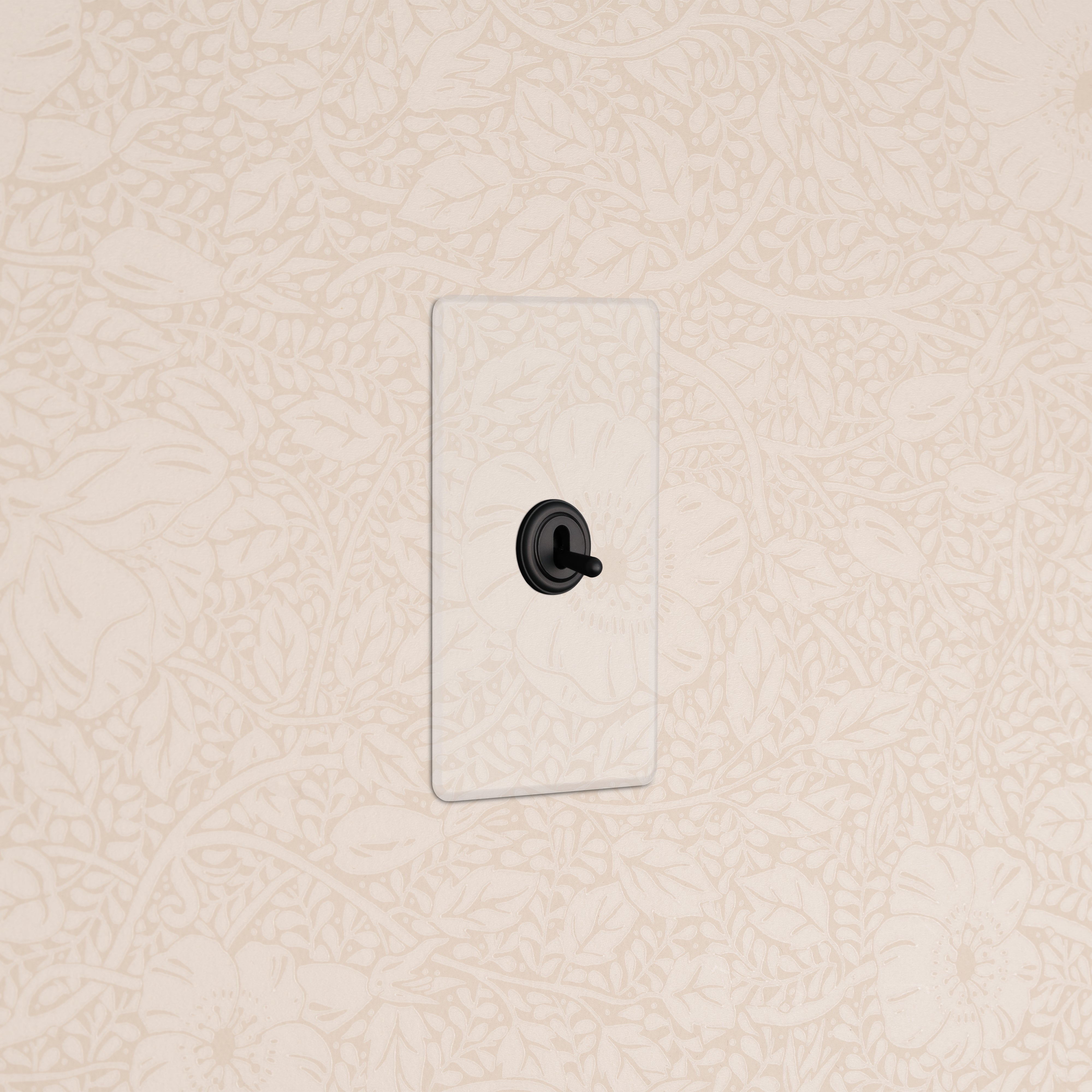 Kew 1G Toggle Switch with a clear bronze cover plate, mounted on a beige wall with a floral pattern.