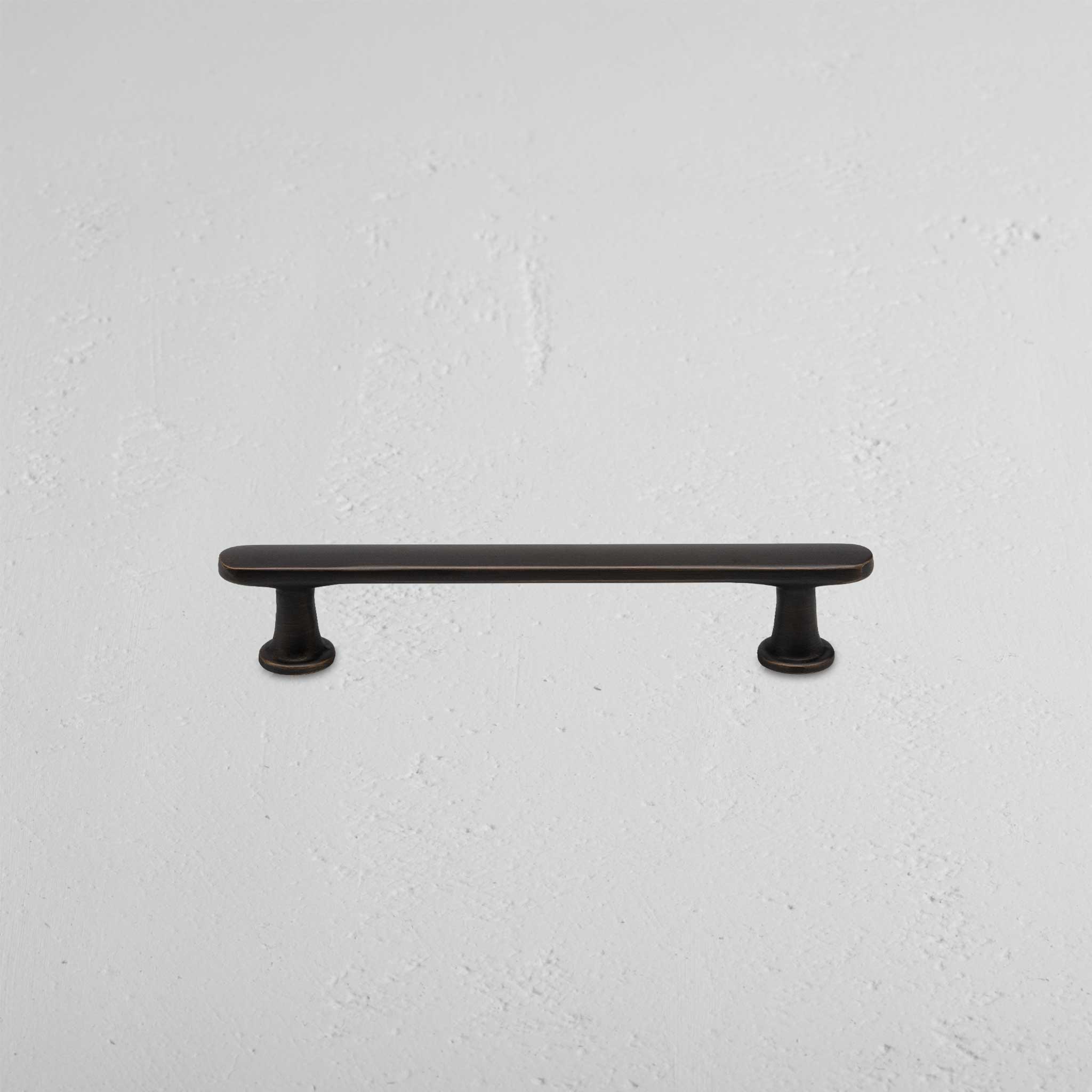 Small bronze Milliner furniture handle with two round bases, mounted on a textured light gray surface.