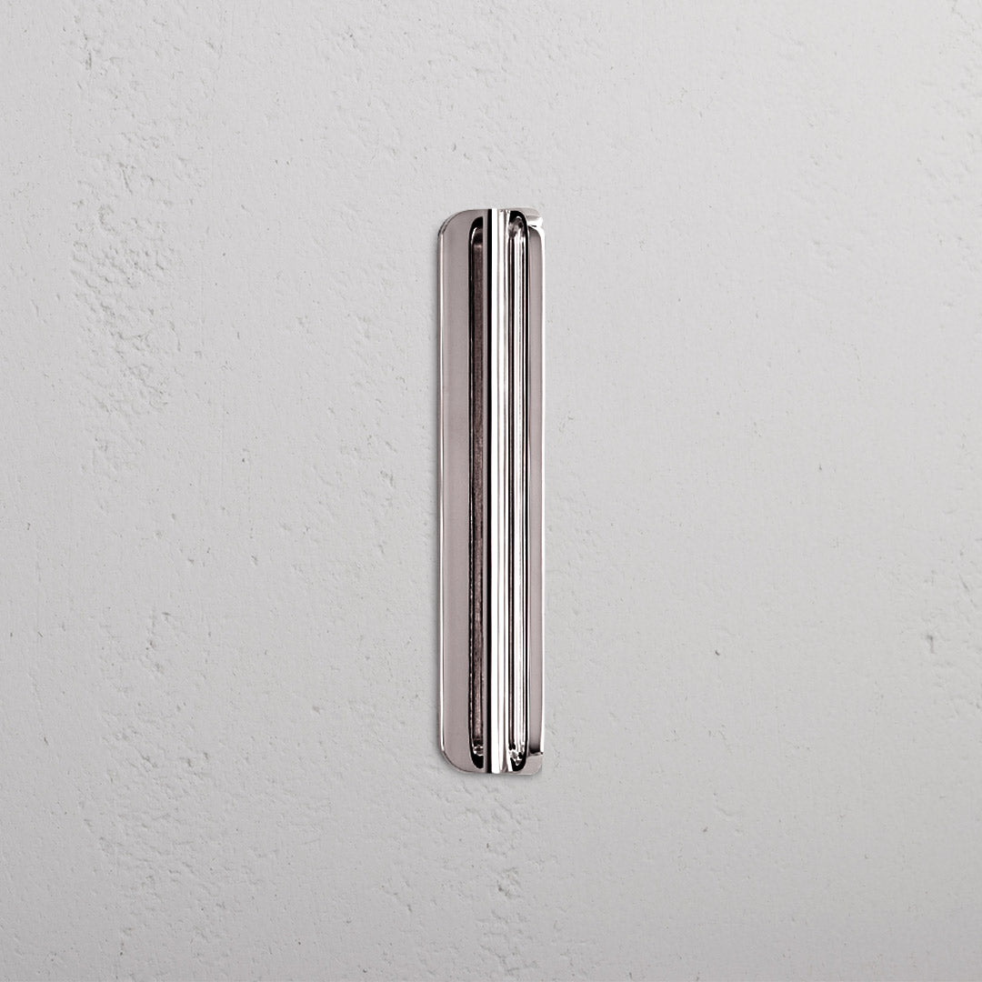 Small polished nickel Oxford furniture handle mounted vertically on a light textured white surface.