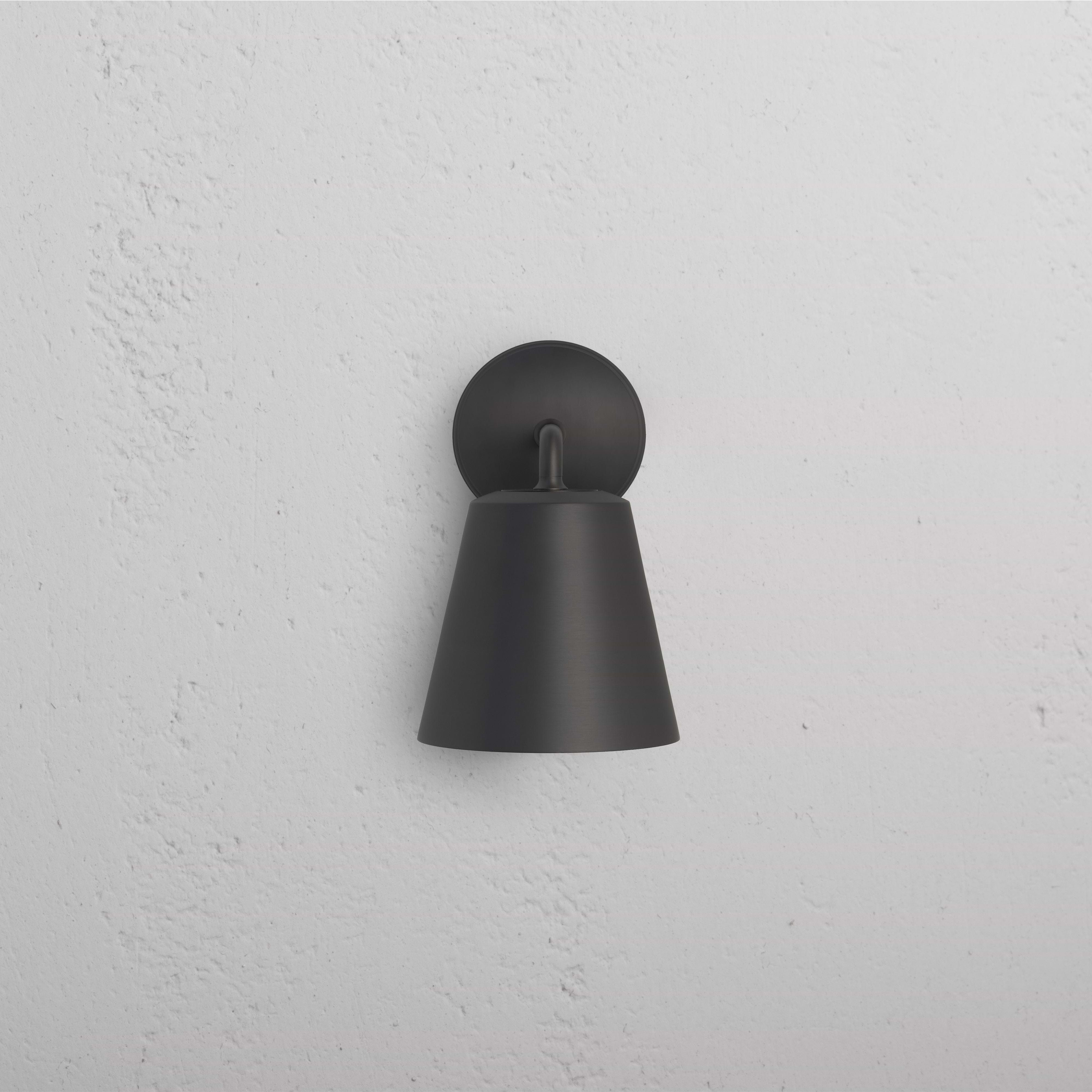 Richmond Medium Wall Light in bronze finish with a conical shade, mounted on a white textured wall.