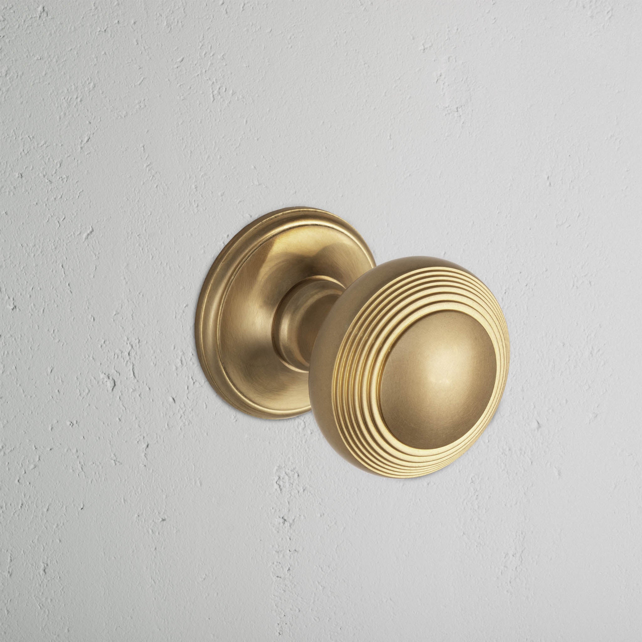 Antique Brass Poplar Unsprung Passage Door Knob Set with ridged circular design mounted on white wall.