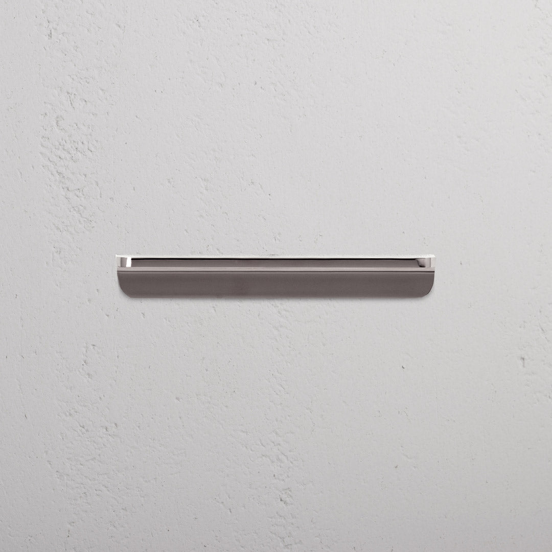 Small polished nickel Oxford furniture handle mounted horizontally on a white textured wall. Minimalist design.