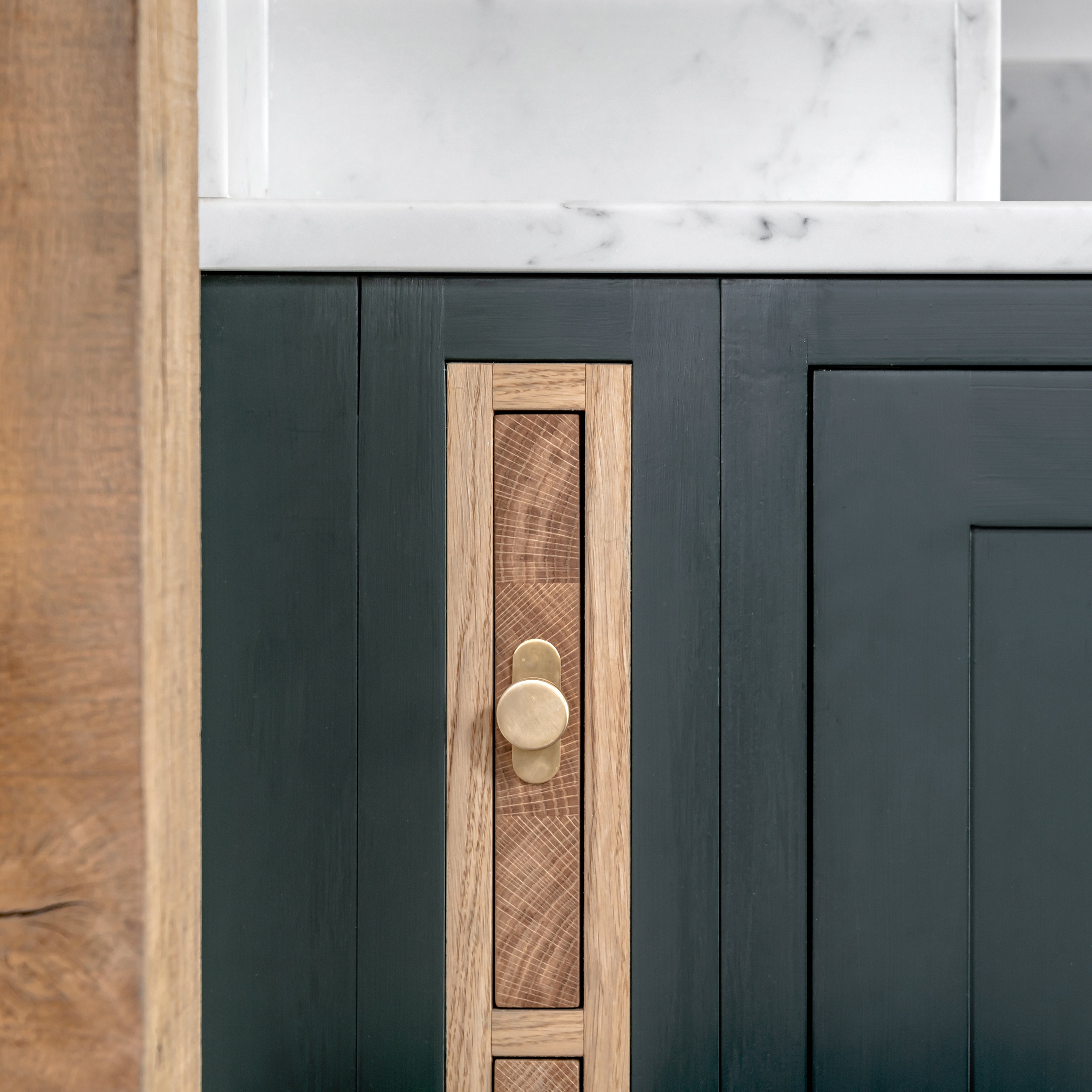 Close-up of a polished Kilburn Furniture Knob mounted on a dark green cabinet door with wood inlay.