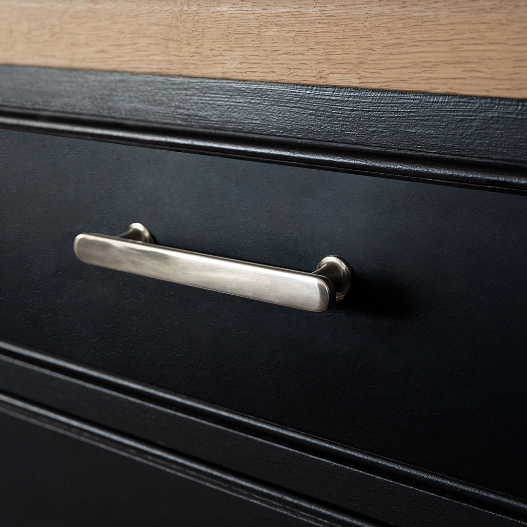 Close-up of a small polished nickel Milliner Furniture Handle attached to a black drawer.