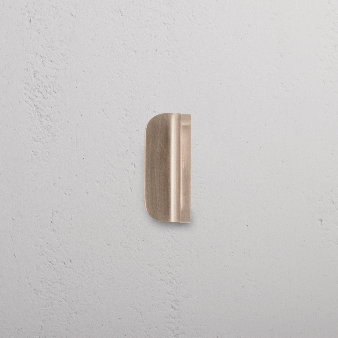 Oxford Furniture Handle Extra Small in antique brass with vertical ridge detail, mounted on a white wall.