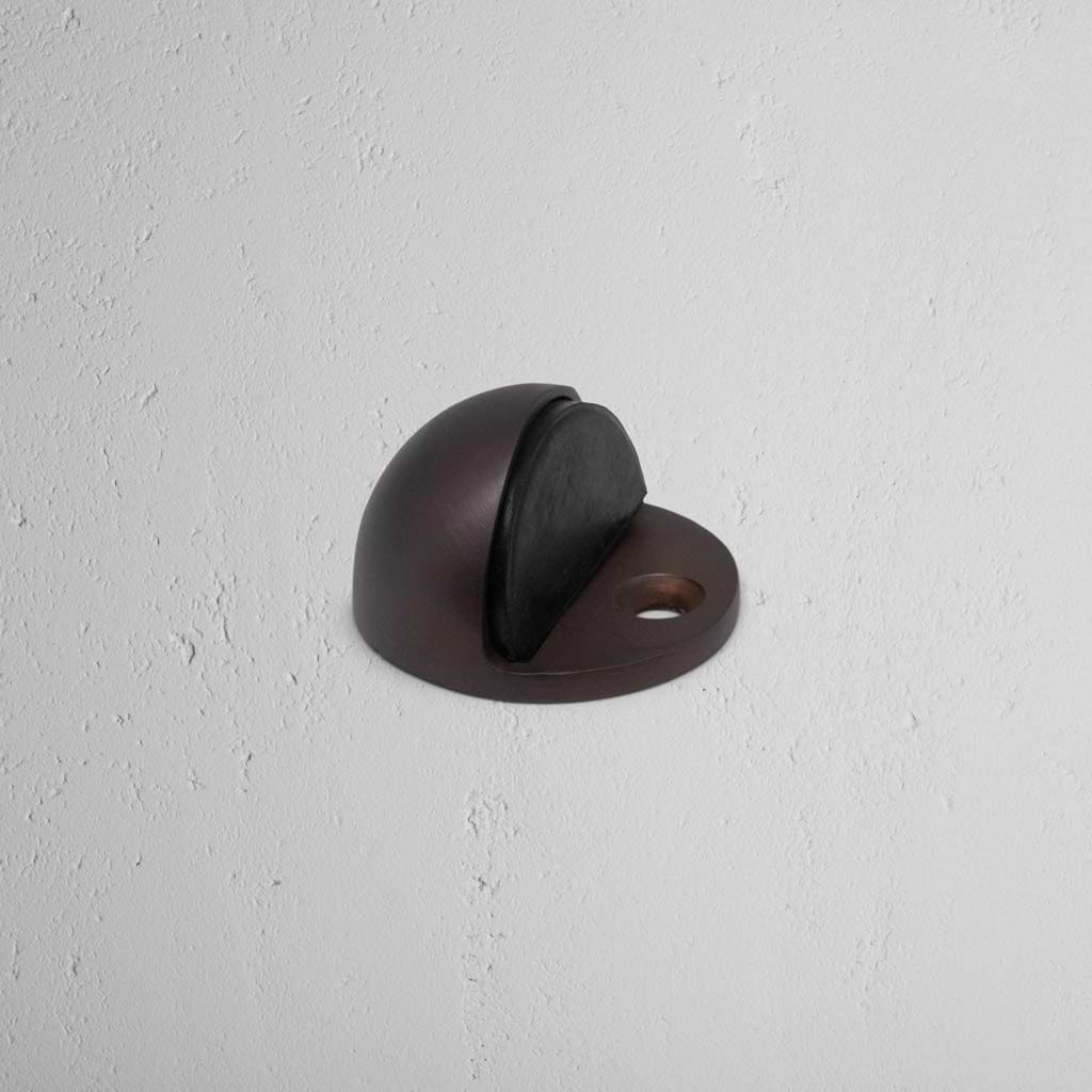 Clifton Half Moon Door Stop in bronze finish with rubber bumper, mounted on a light wall.