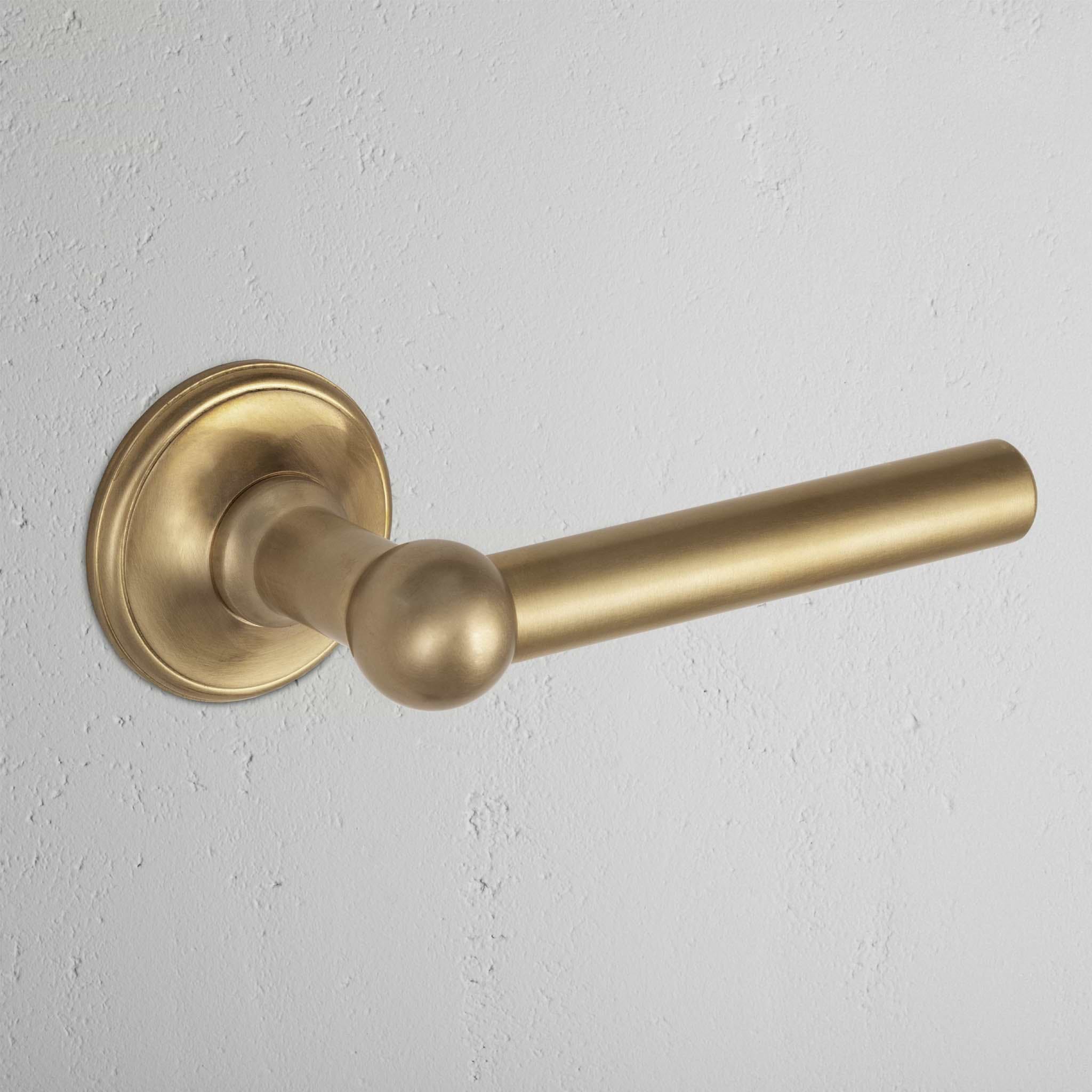 Harper Passage Door Handle Set in antique brass with a round baseplate, mounted on a white wall.