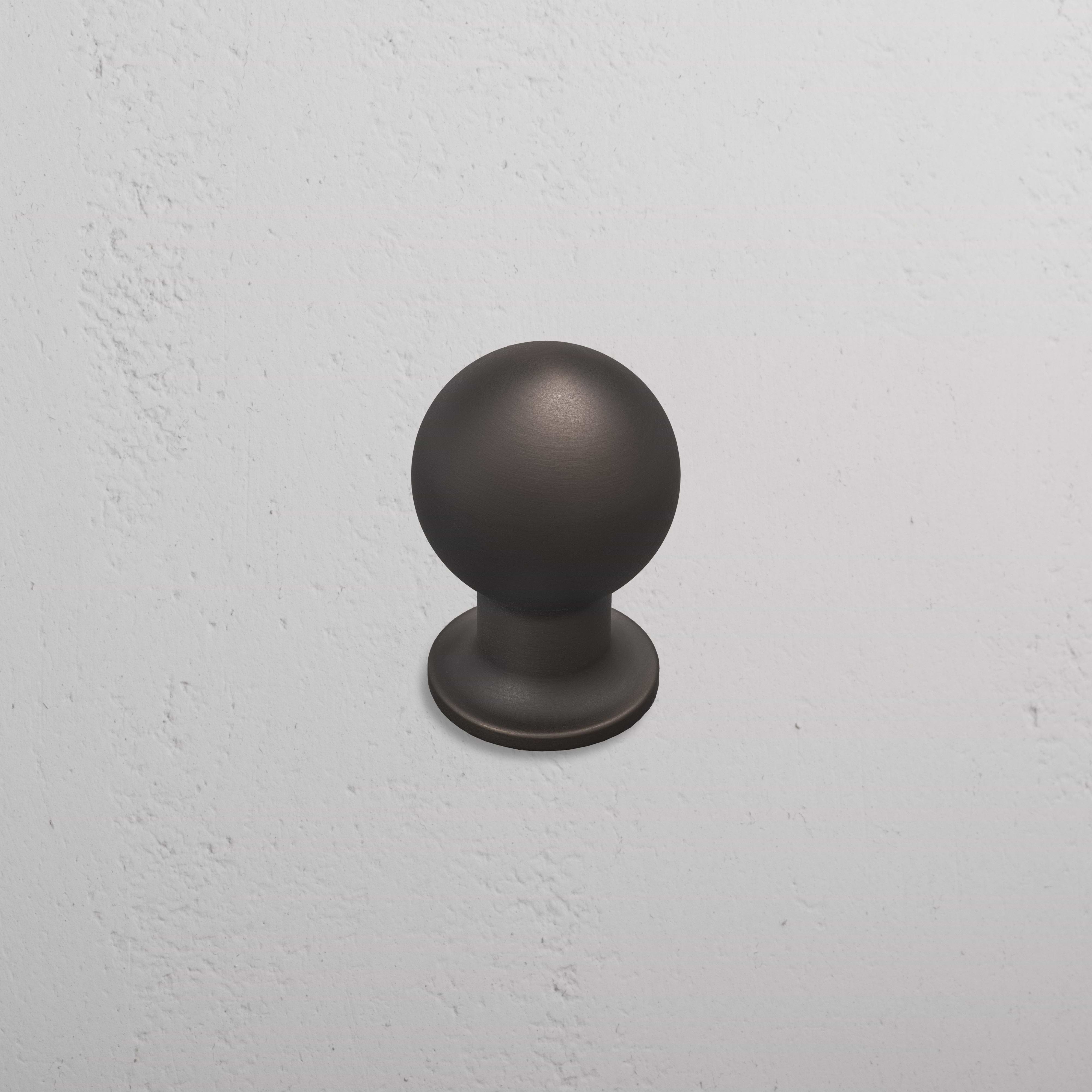 Medium-sized Bayswater Furniture Knob in matte bronze, mounted on a textured white wall.