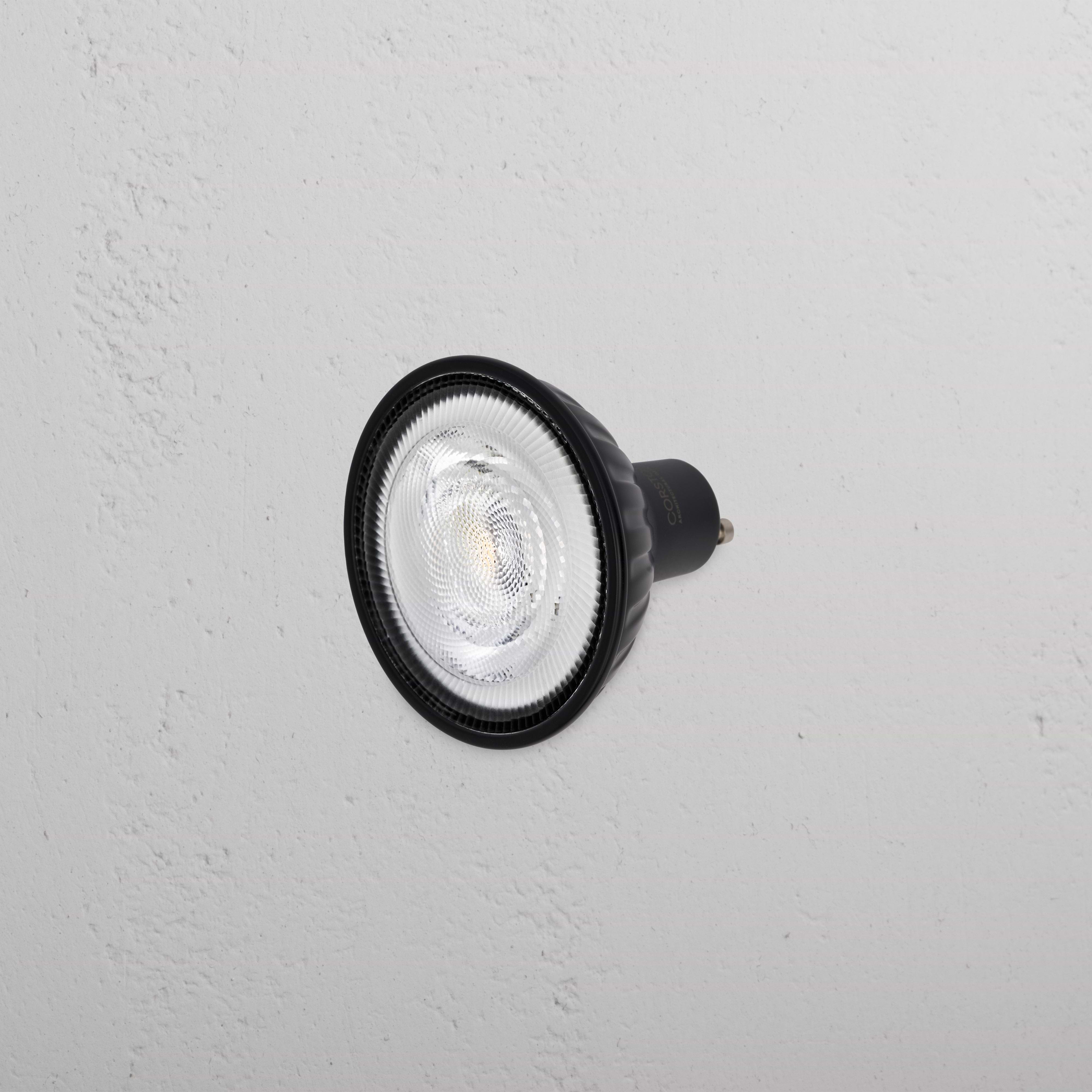 Arthur 11W 70mm LED GU10 24° Bulb in black, shown mounted on a white wall, lens facing outward.