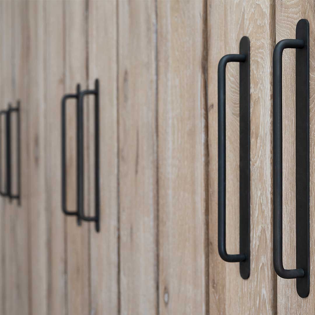 Kilburn Furniture Handle Medium in bronze, mounted on light wood cabinet doors in a modern arrangement.
