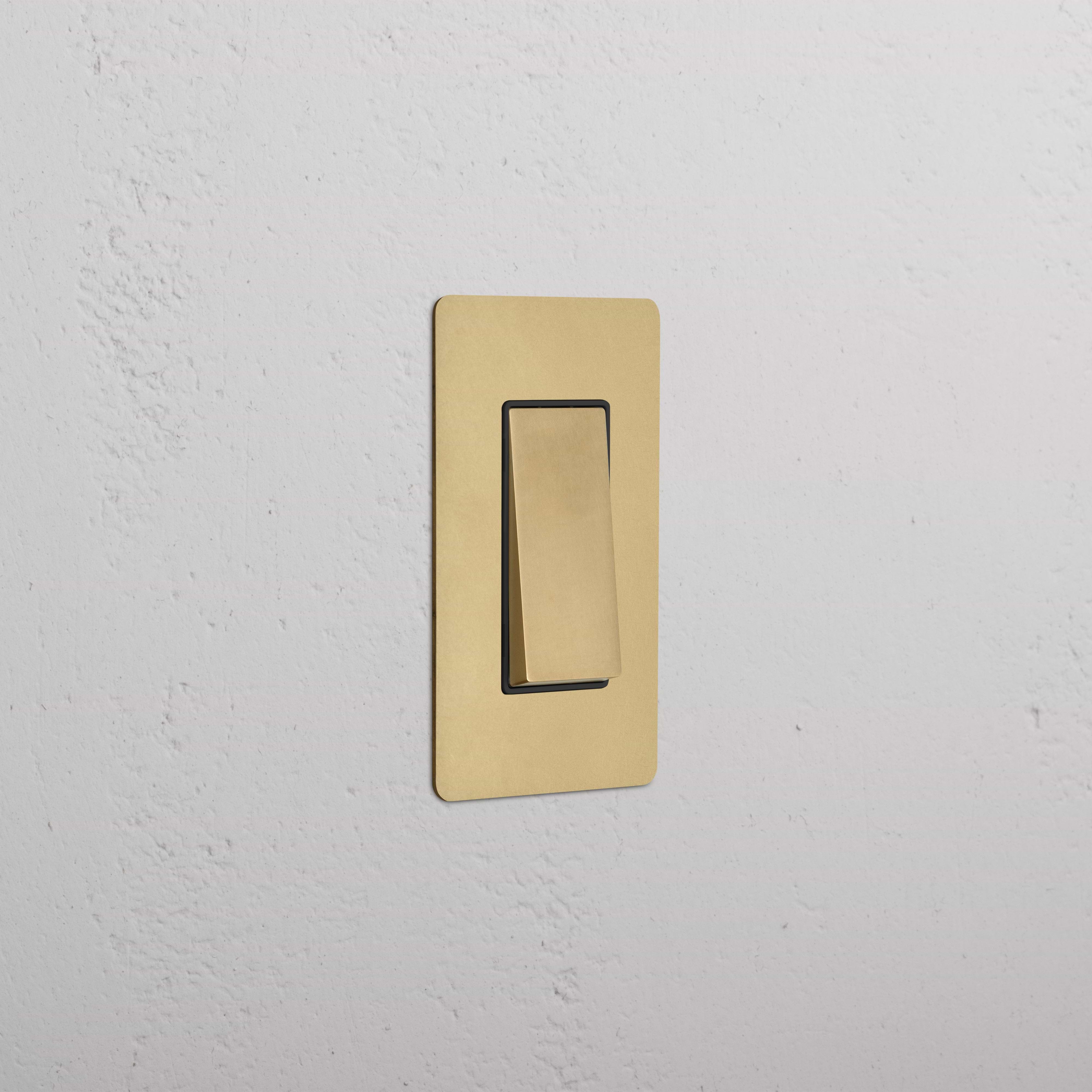 Kew 1G Rocker Switch in Antique Brass Black finish, shown installed on a white wall, switch off.