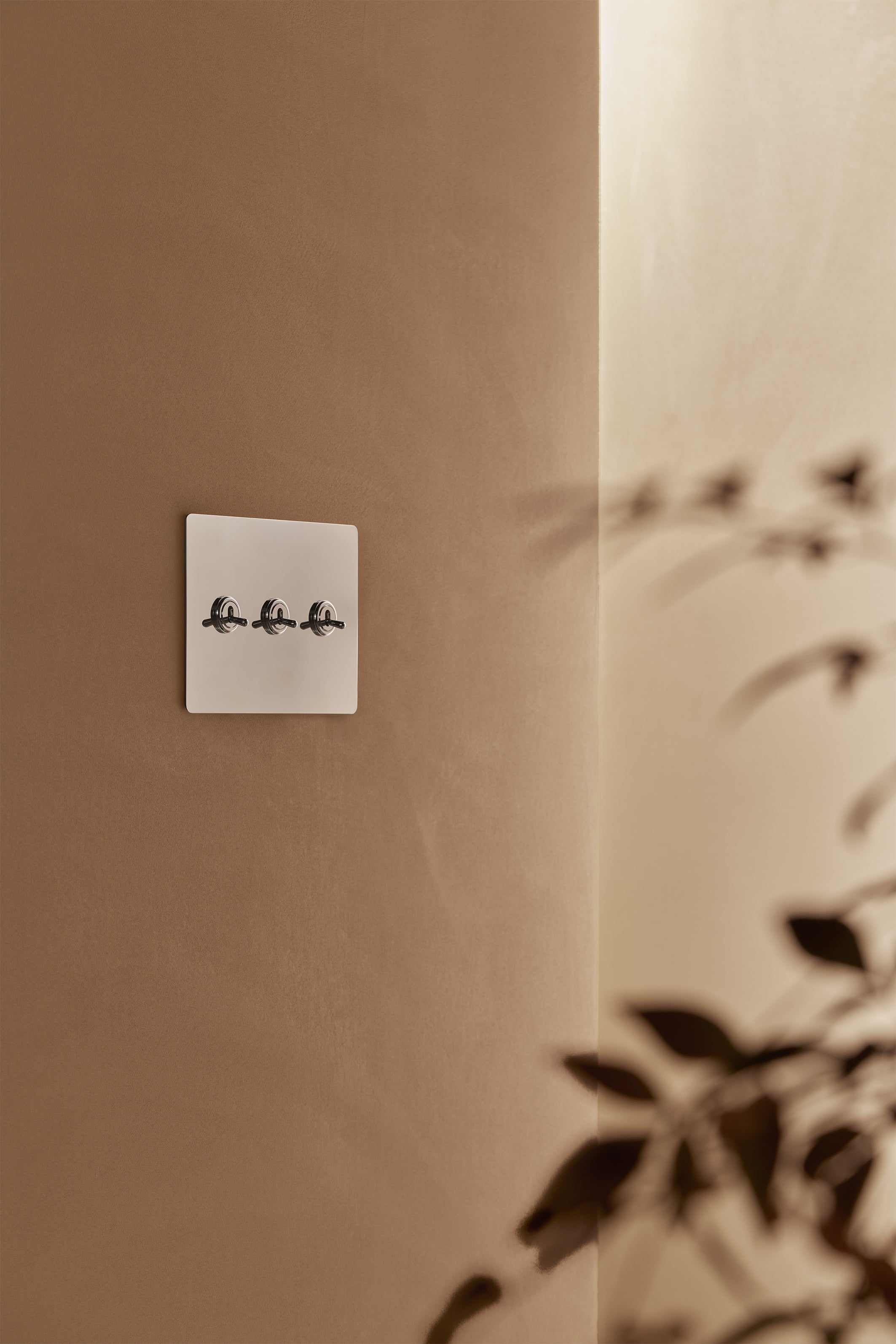 Kew 3G Toggle Switch in polished nickel, mounted on a wall with a warm beige background and soft shadows.