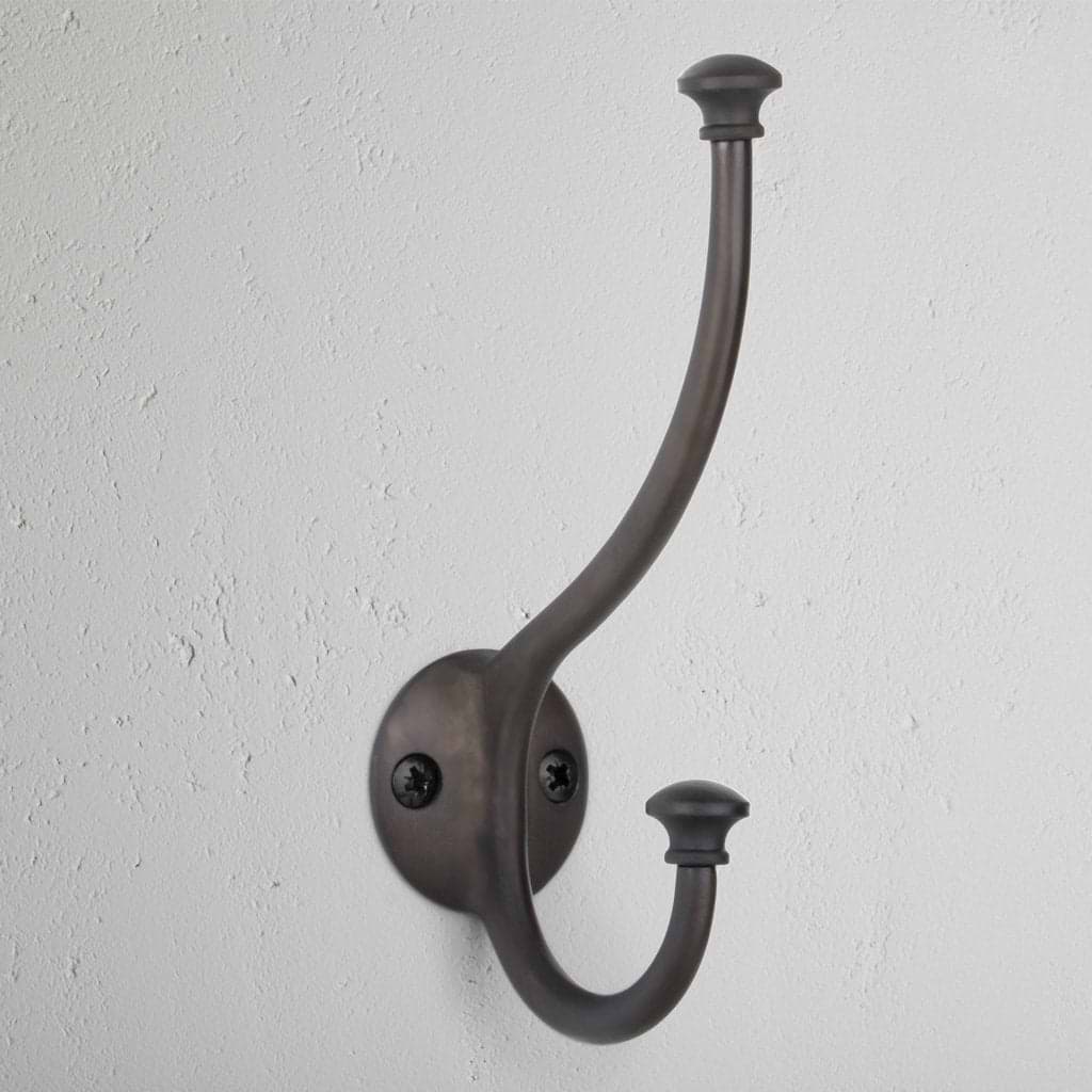 Bronze Mews Hook wall-mounted coat hook with two prongs, attached to a white textured wall.