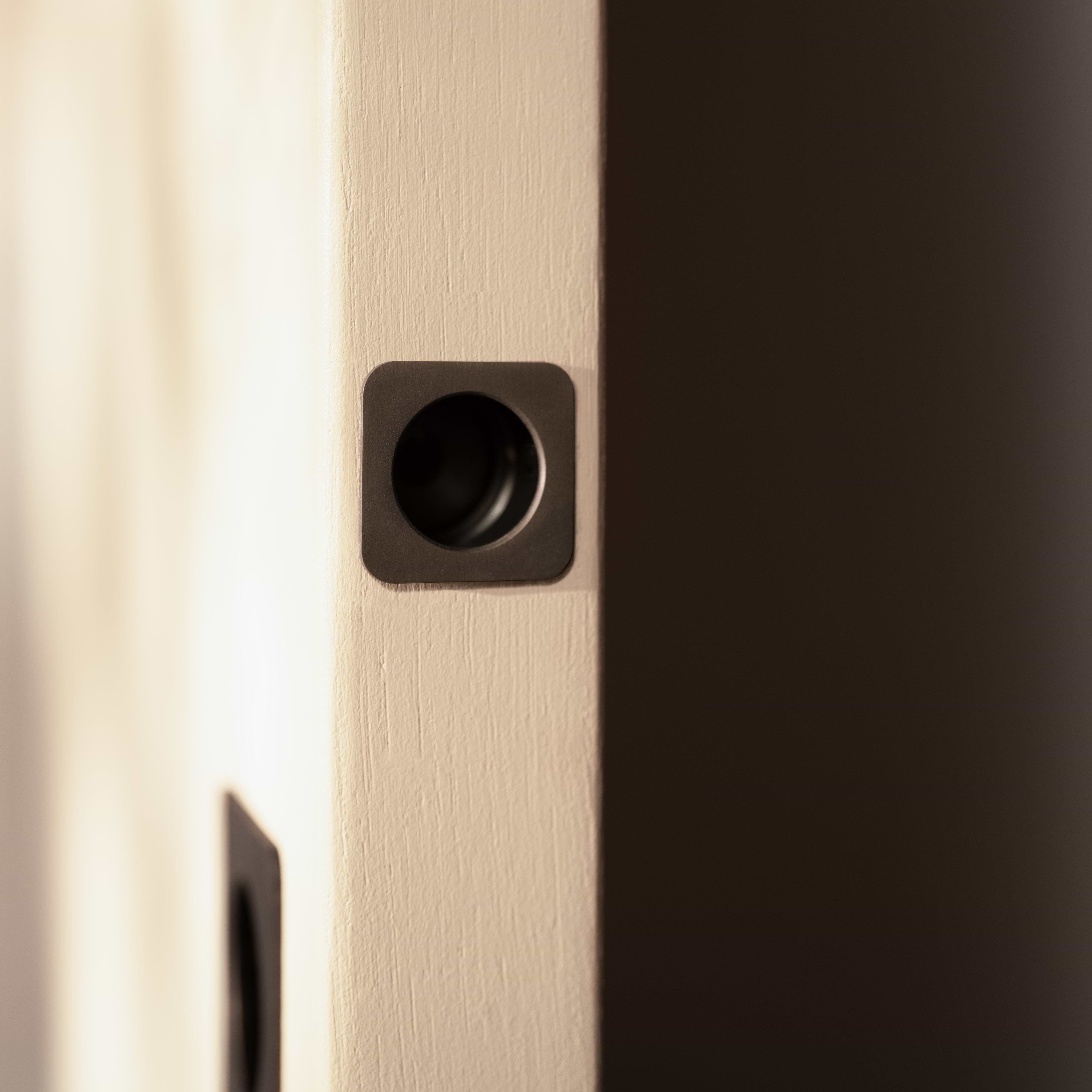 Close-up of a Regent Recessed Edge Pull in bronze installed on the edge of a light-colored door.