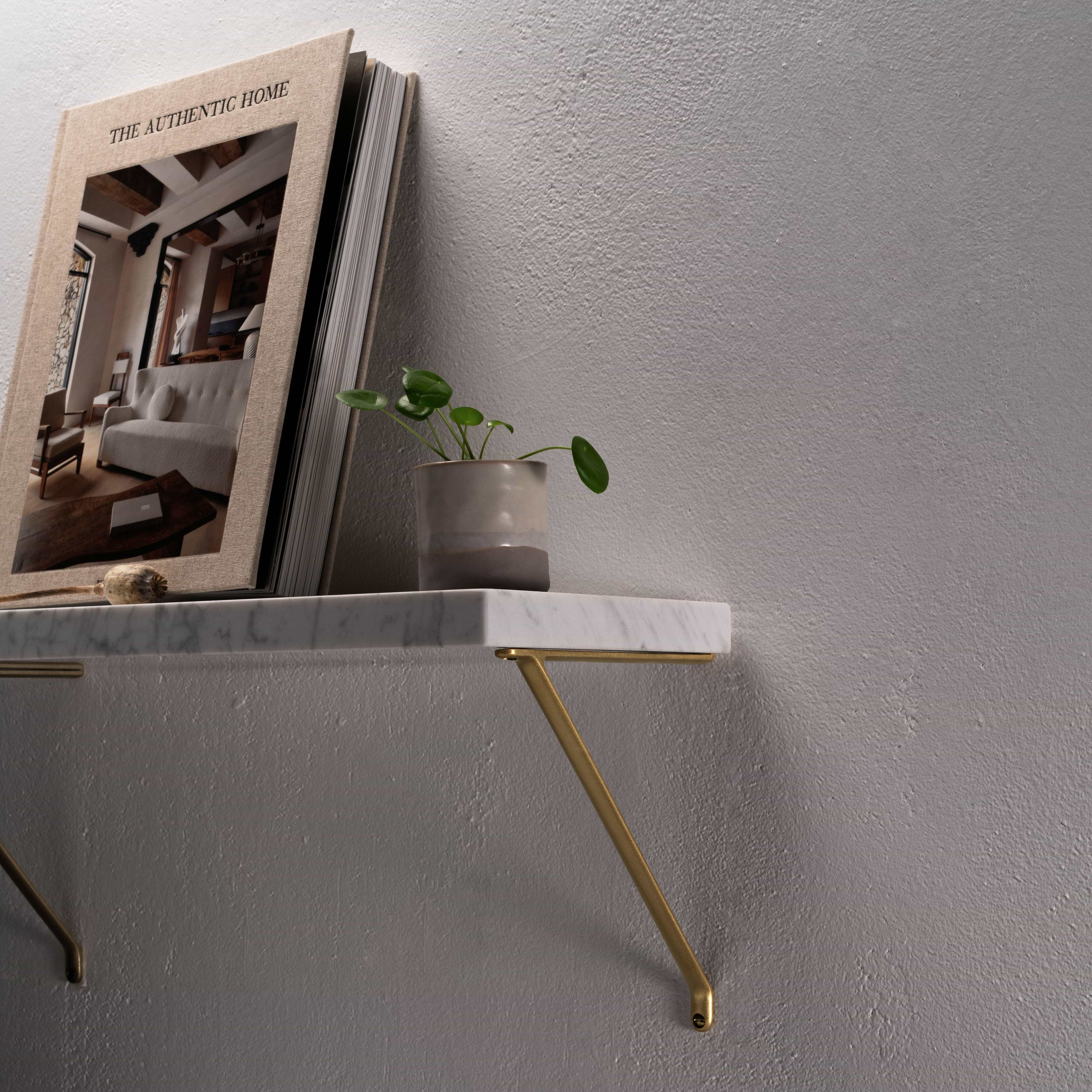 Medium Brixton Shelf Bracket in Antique Brass supporting a marble shelf against a light gray textured wall.