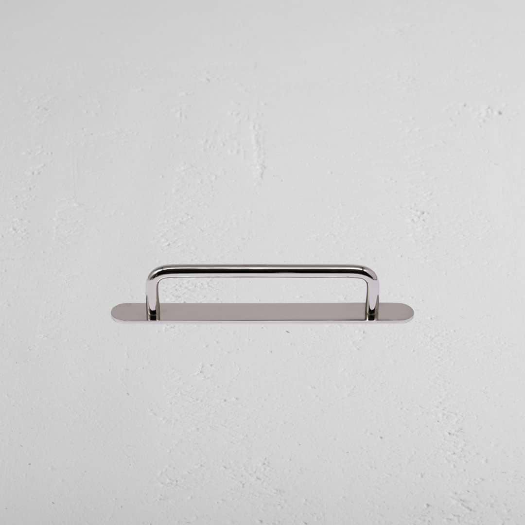 Kilburn Furniture Handle Small in polished nickel, mounted horizontally on a white textured wall.