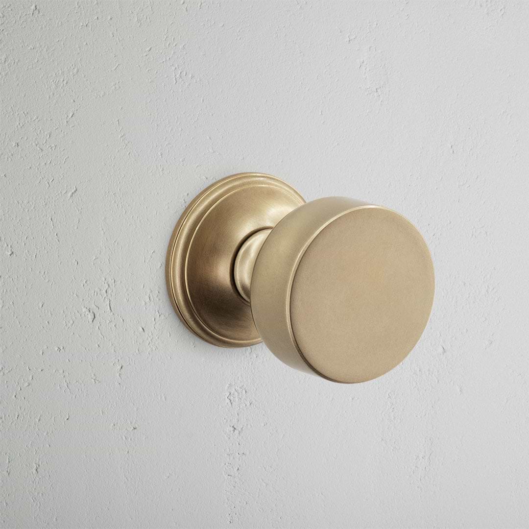 Onslow Dummy Door Knob Set in antique brass with a round, smooth finish, mounted on a light gray wall.