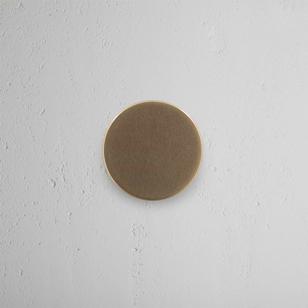 Onslow Dummy Door Knob Set in Antique Brass, round and flat, mounted on a light gray textured wall.