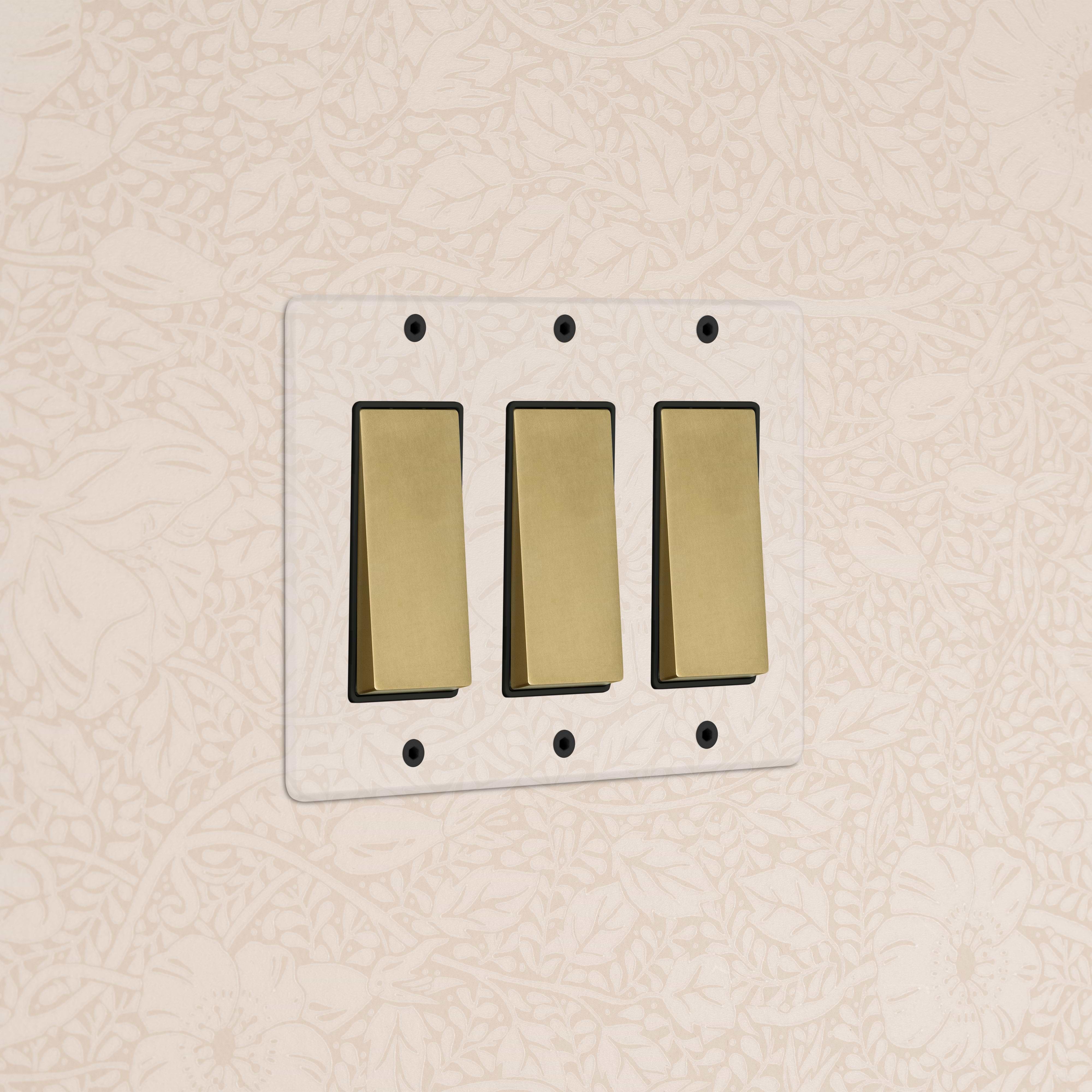 Kew 3G Rocker Switch in clear antique brass with black switches, shown on a wall.