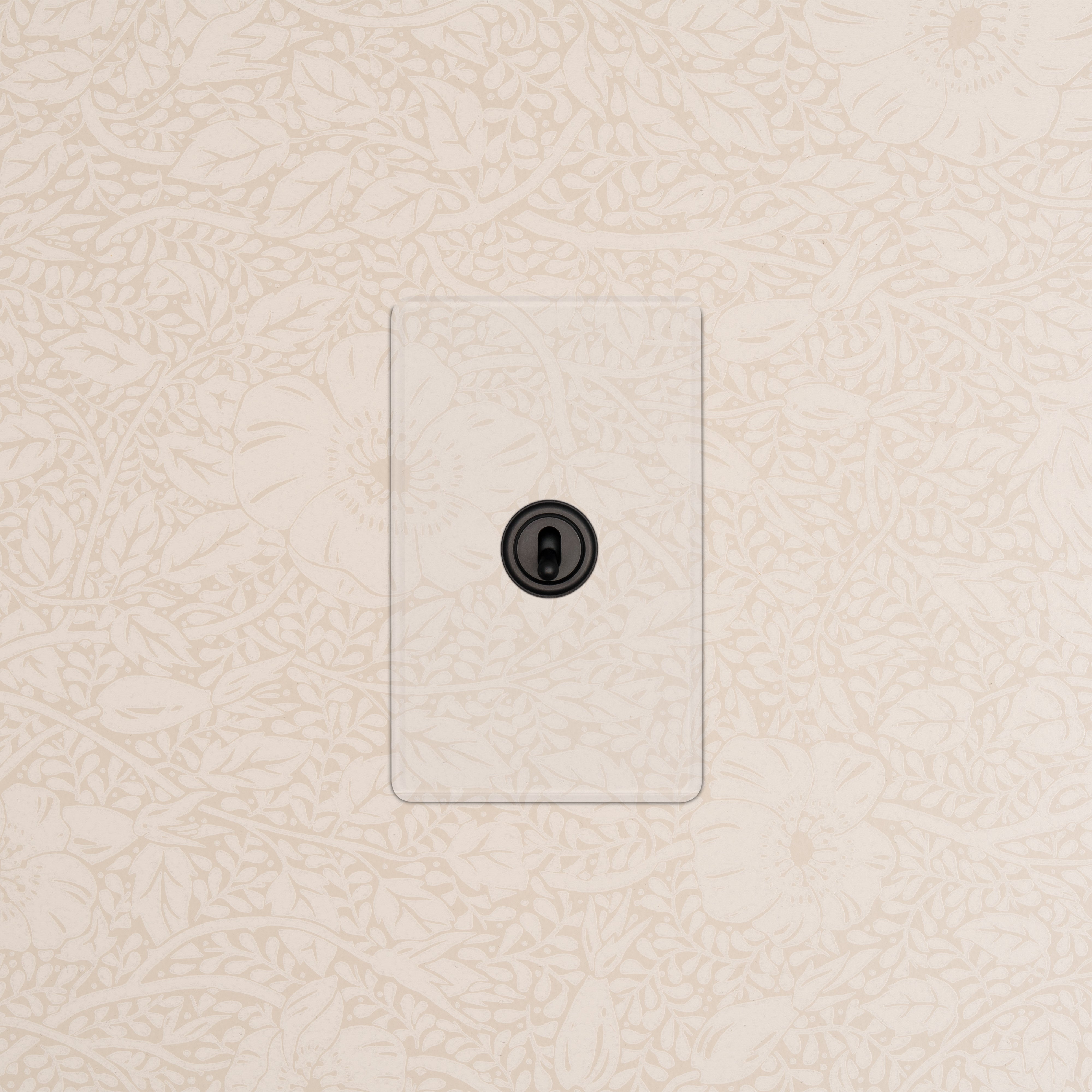 Kew 1G Toggle Switch in Clear Bronze finish, installed on a wall with a light beige floral pattern.
