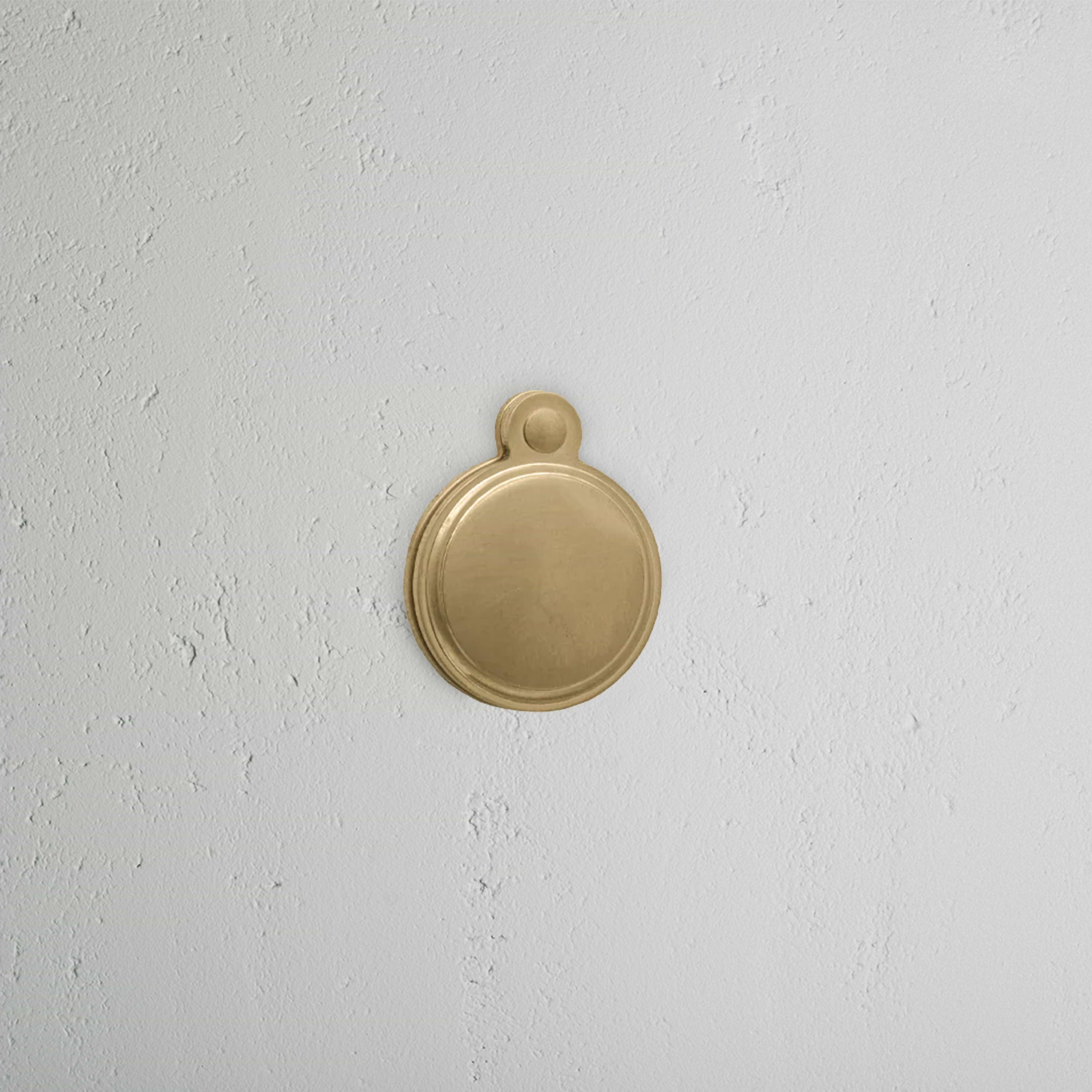 Warwick Covered Key Escutcheon in Antique Brass, a round keyhole cover with a hinged lid on a white wall.