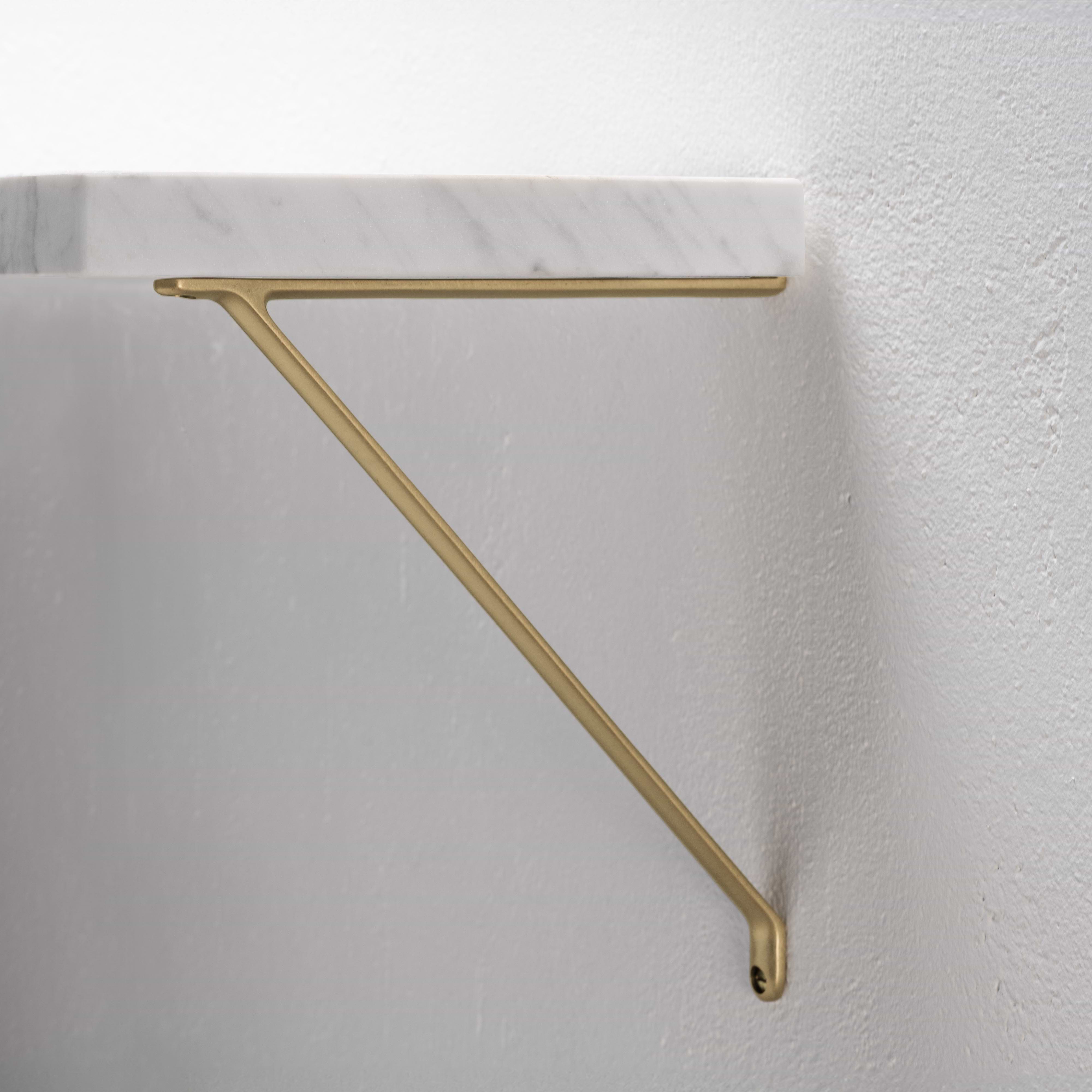 Medium-sized Brixton Shelf Bracket in antique brass, mounted on a white wall and supporting a shelf.