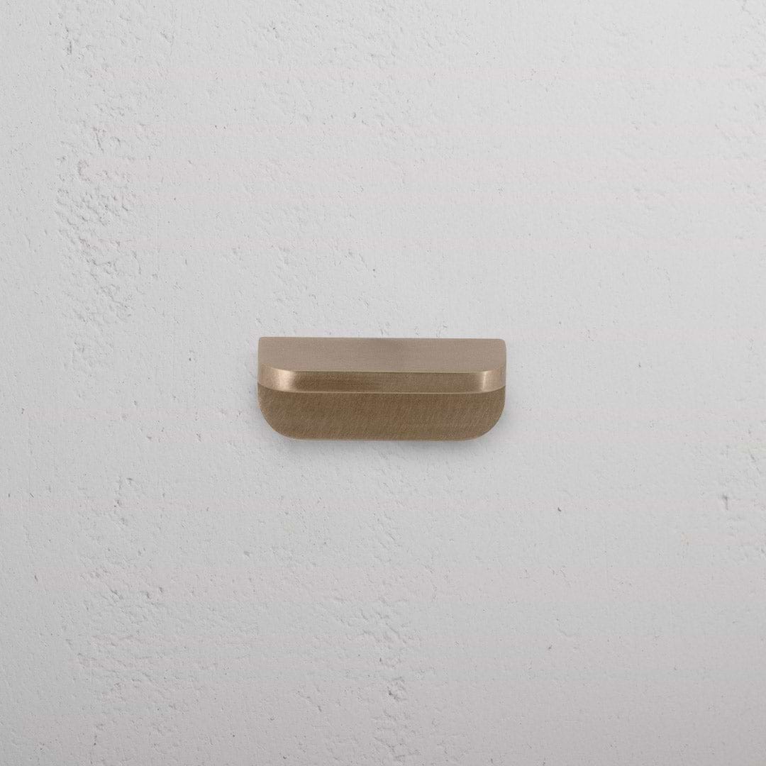 An extra small Oxford furniture handle in antique brass finish, mounted on a white surface.