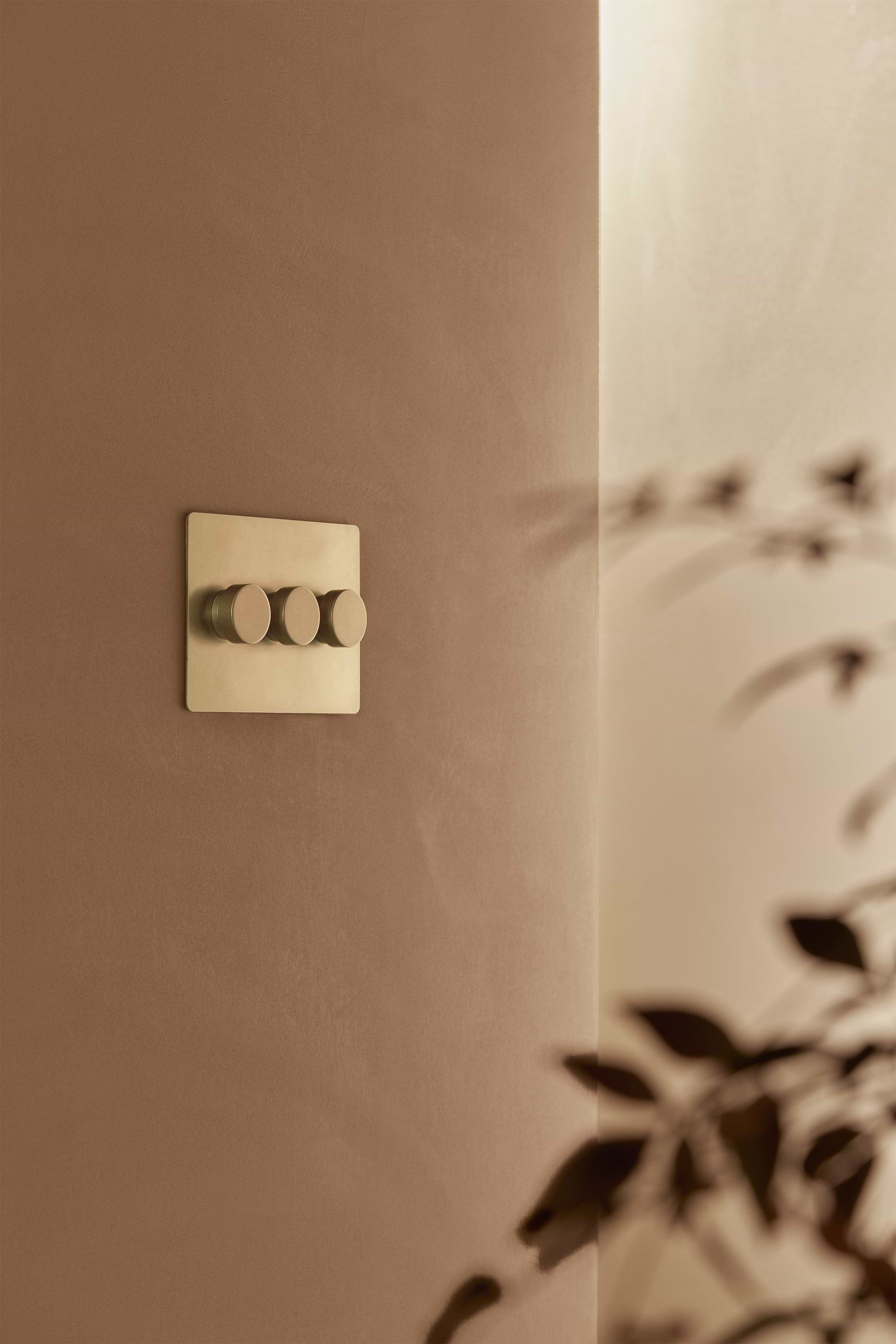 Kew 3G Dimmer Switch in Antique Brass finish with three round knobs mounted on a wall.