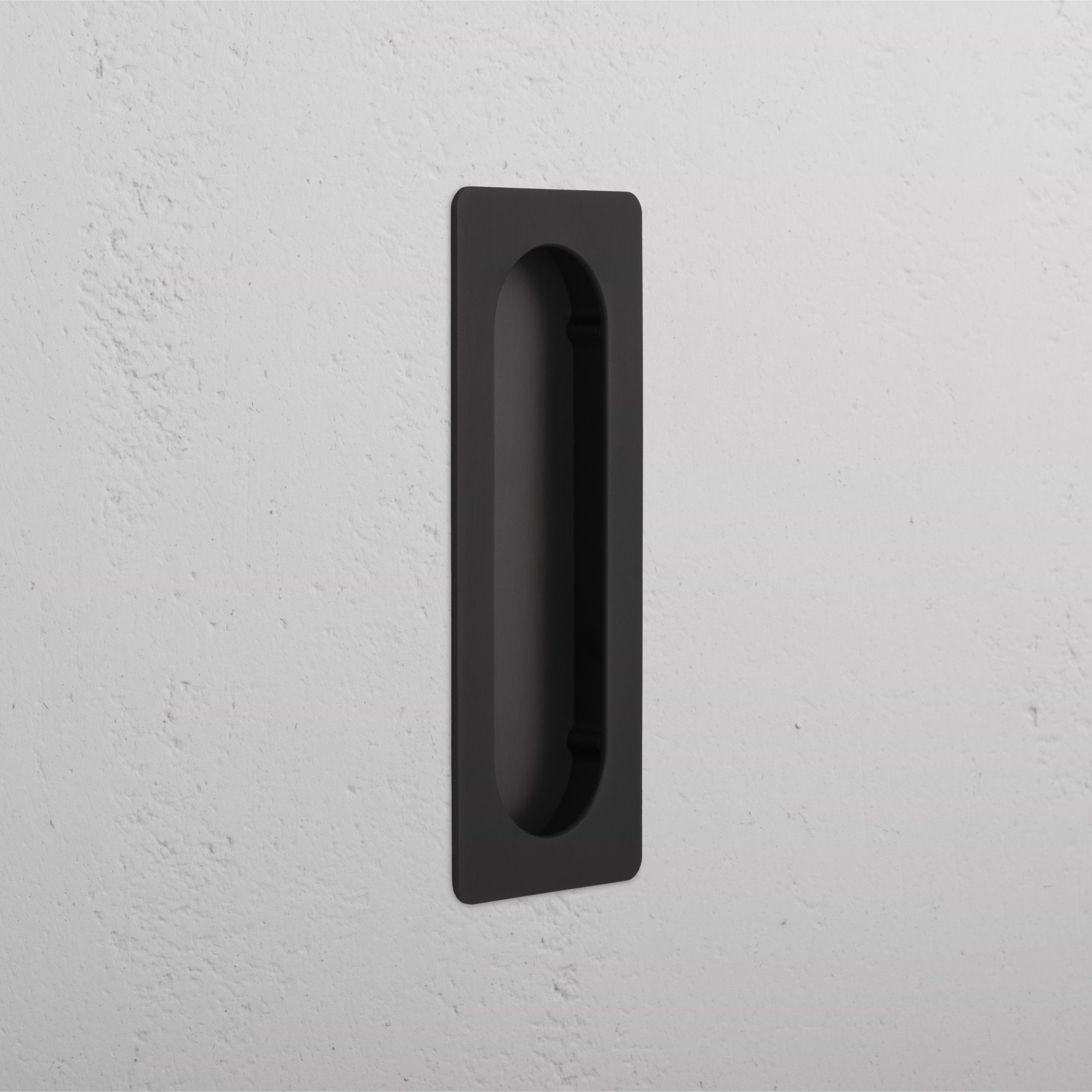 Rectangular Regent Recessed Medium Pull in bronze finish, installed on a white textured wall.
