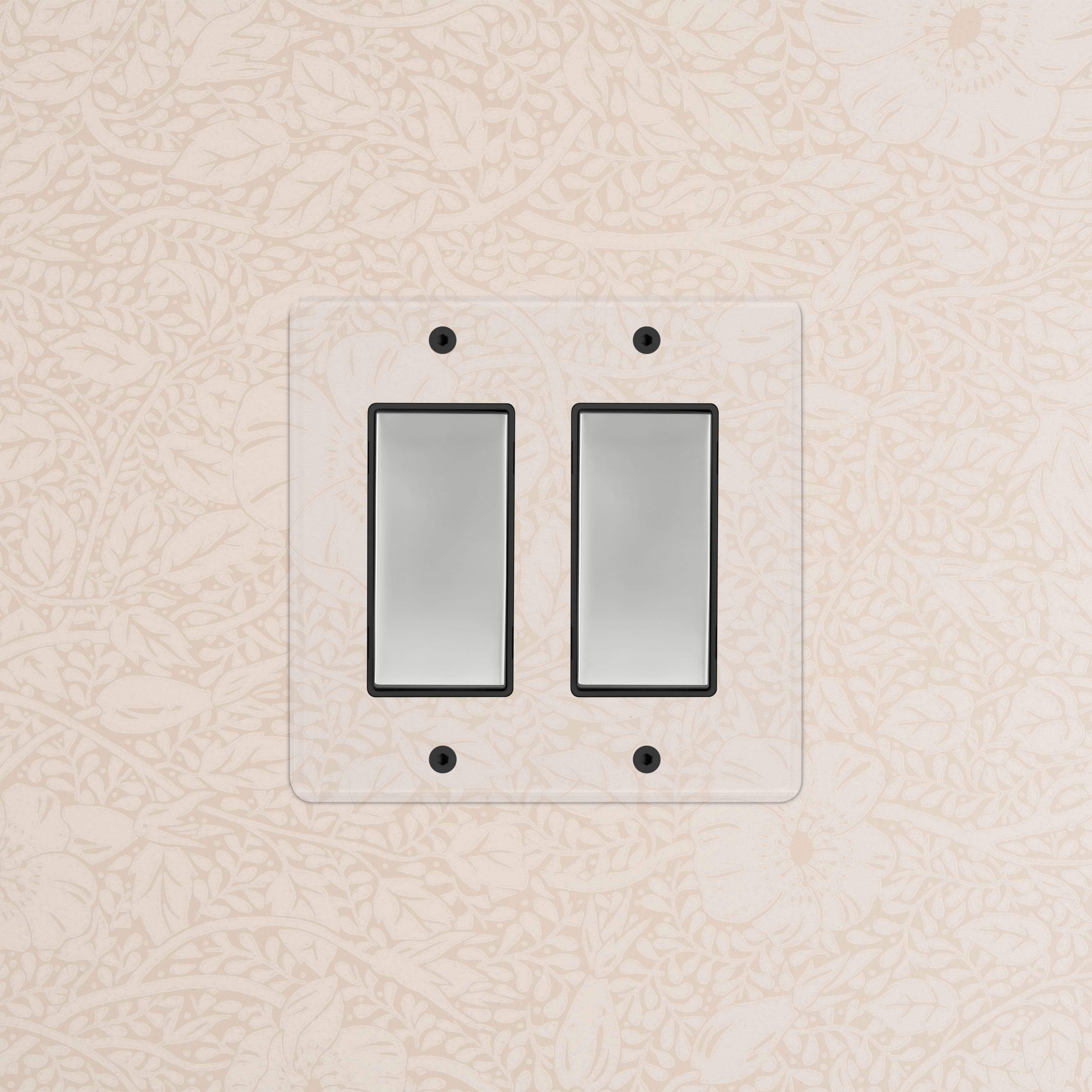 Kew 2G Rocker Switch in clear polished nickel with black trim, mounted on beige floral wallpaper.