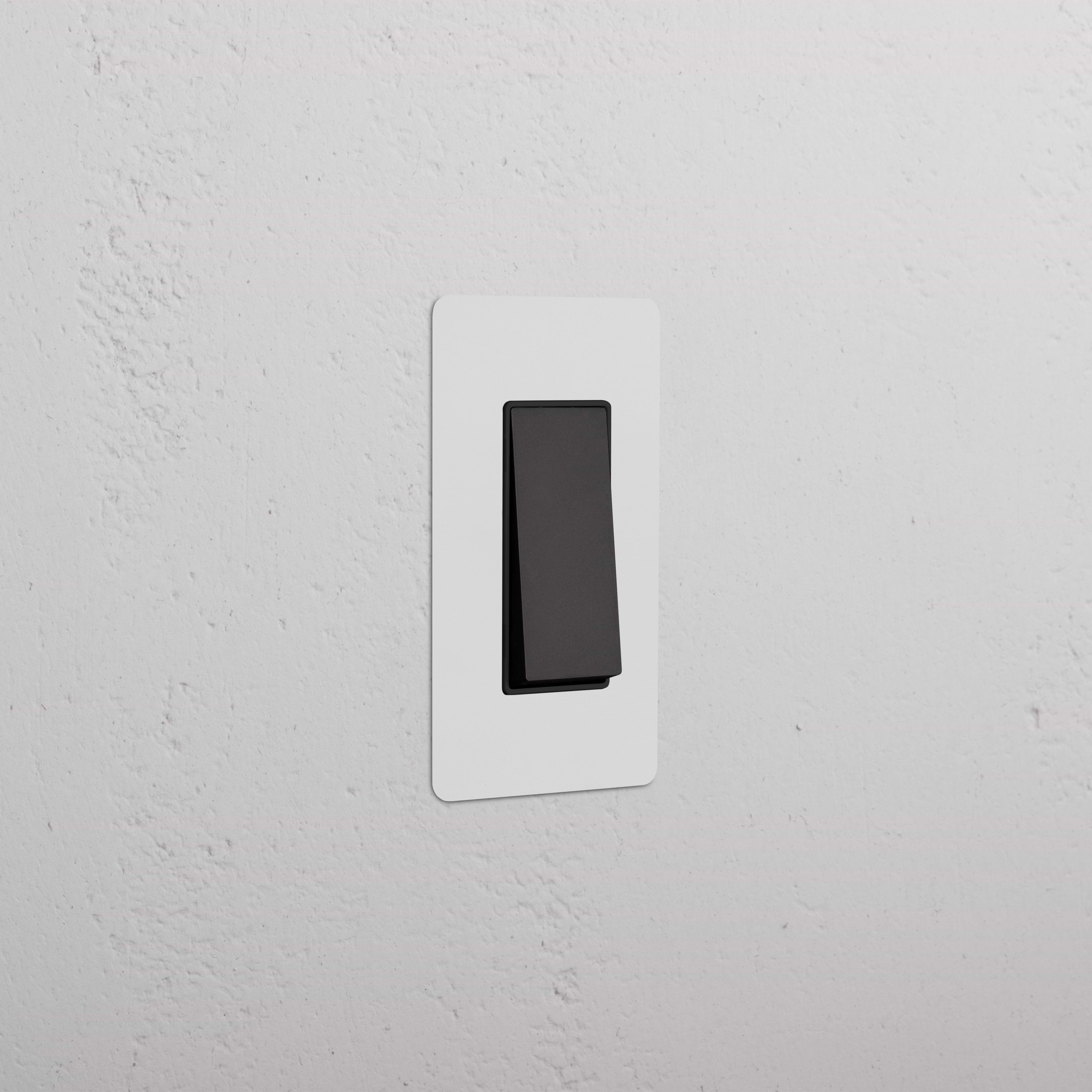 Kew 1G Retractive Rocker Switch in paintable bronze black finish, installed on a white wall plate.