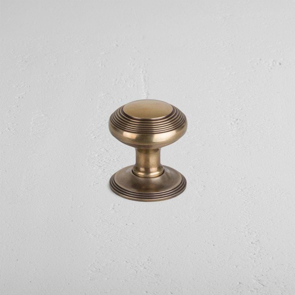 Poplar Passage Door Knob Set in Antique Brass, featuring a round knob with decorative ridges, on a light surface.