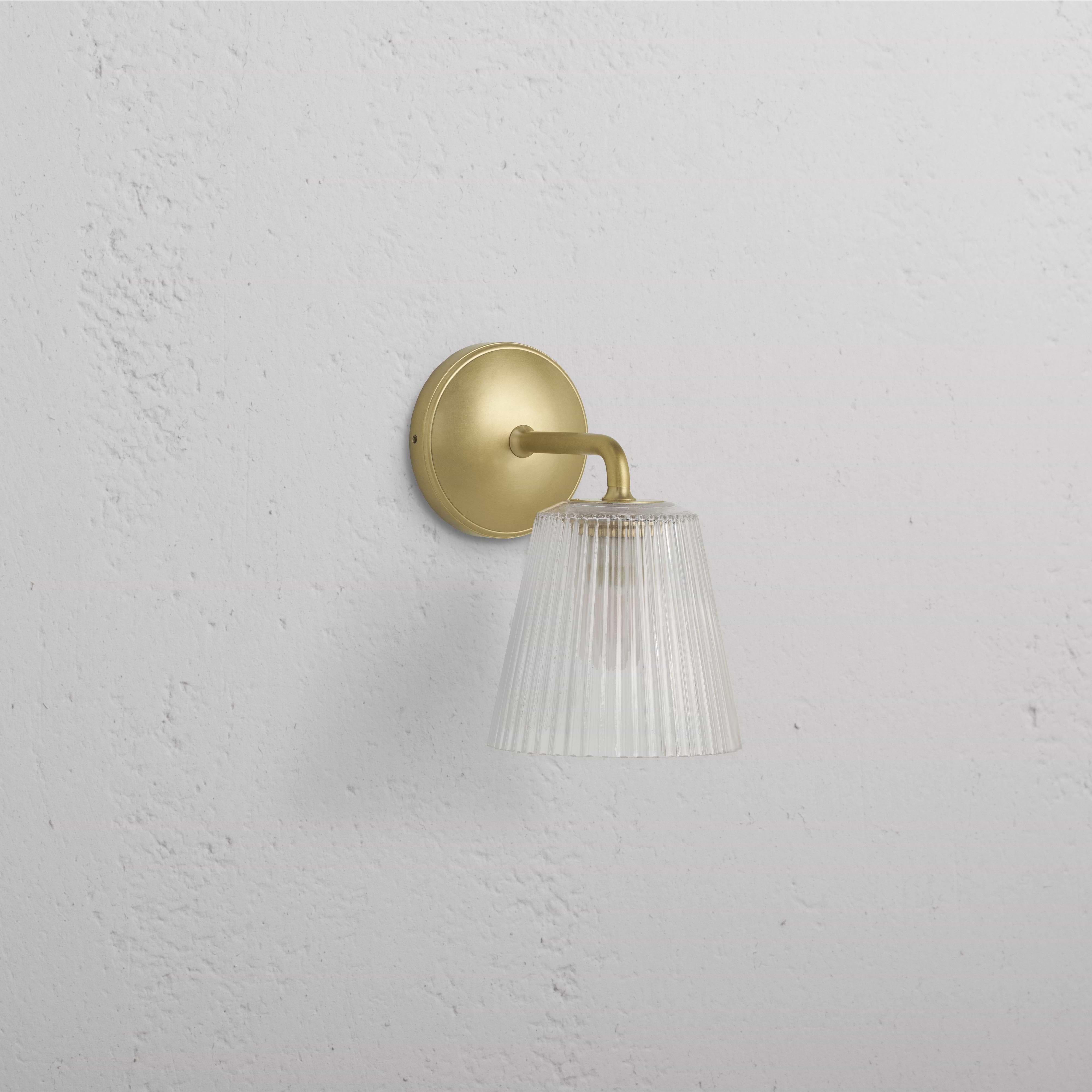Richmond Medium Wall Light with fluted clear glass shade and antique brass base mounted on a white wall.