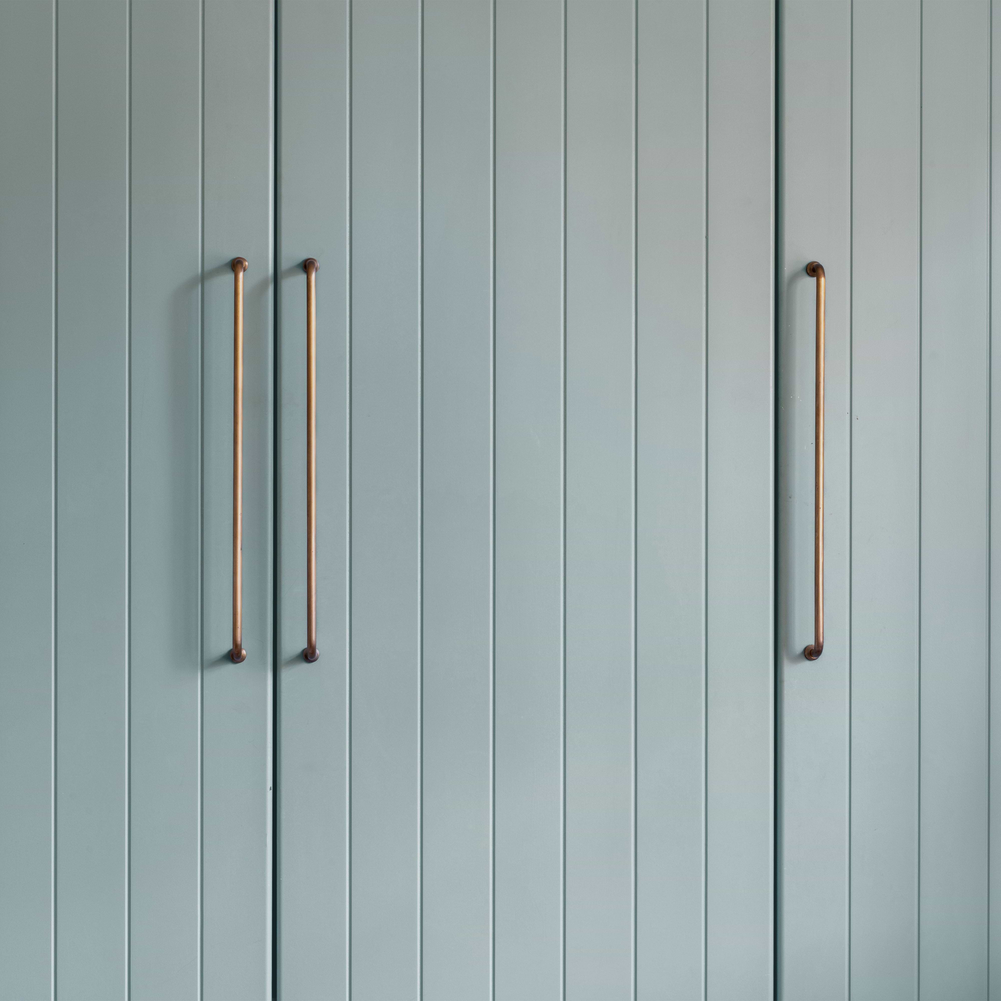 Large Sycamore Furniture Handle in antique brass fitted to light blue paneled cabinet doors, arranged in pairs.