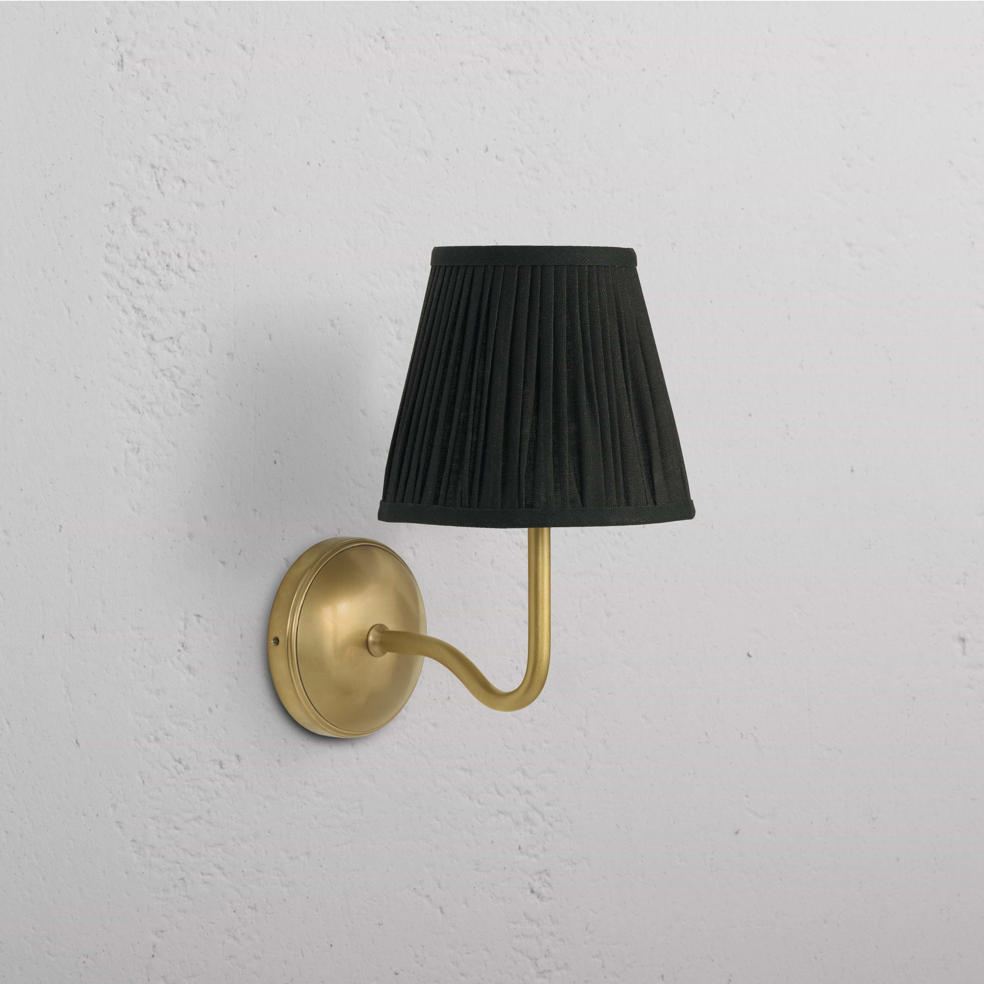 Malvern Medium Wall Light in Deep Green with antique brass finish and curved arm, mounted on a white wall.