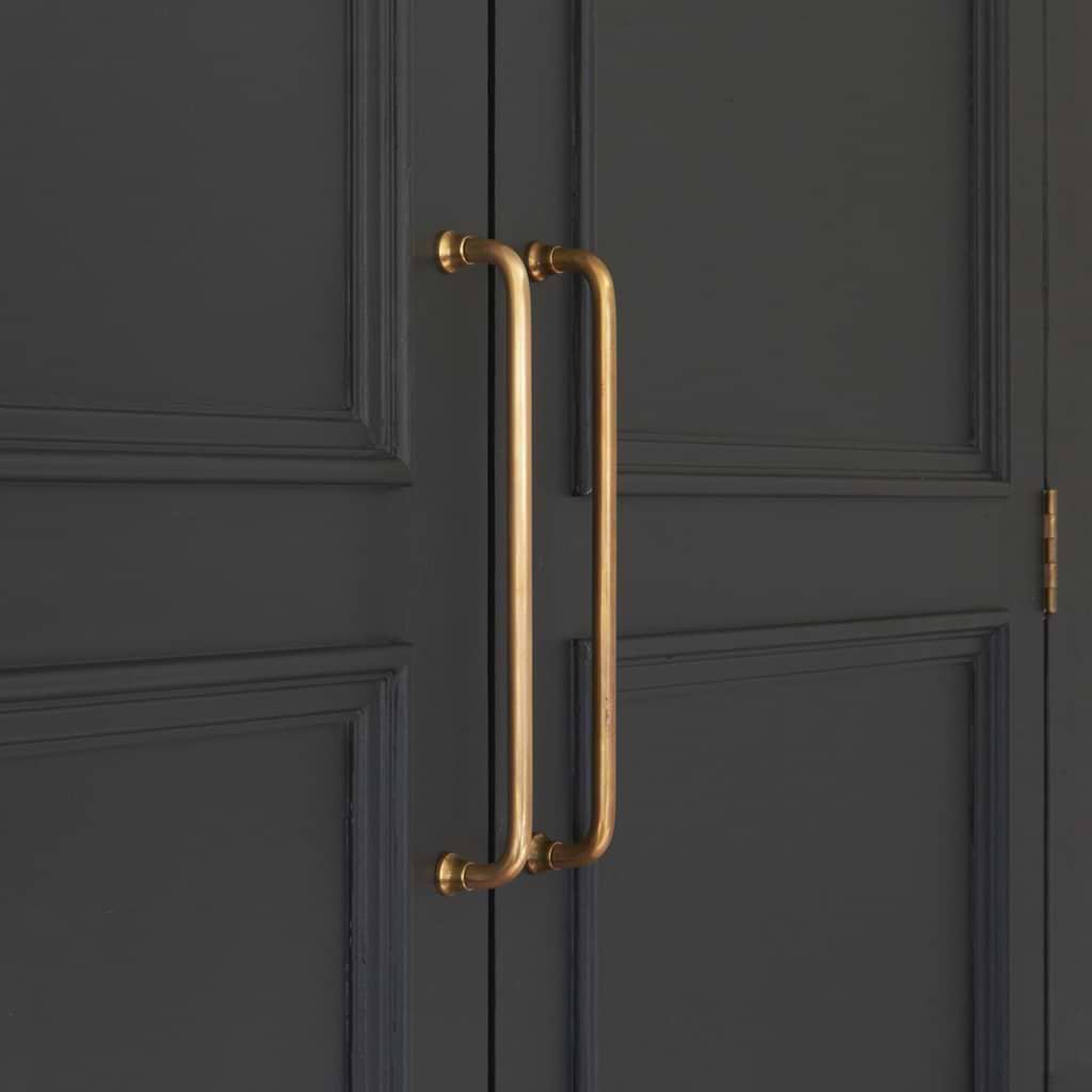 Close-up of two Sycamore Furniture Handle Mediums in Antique Brass on dark, paneled double doors.