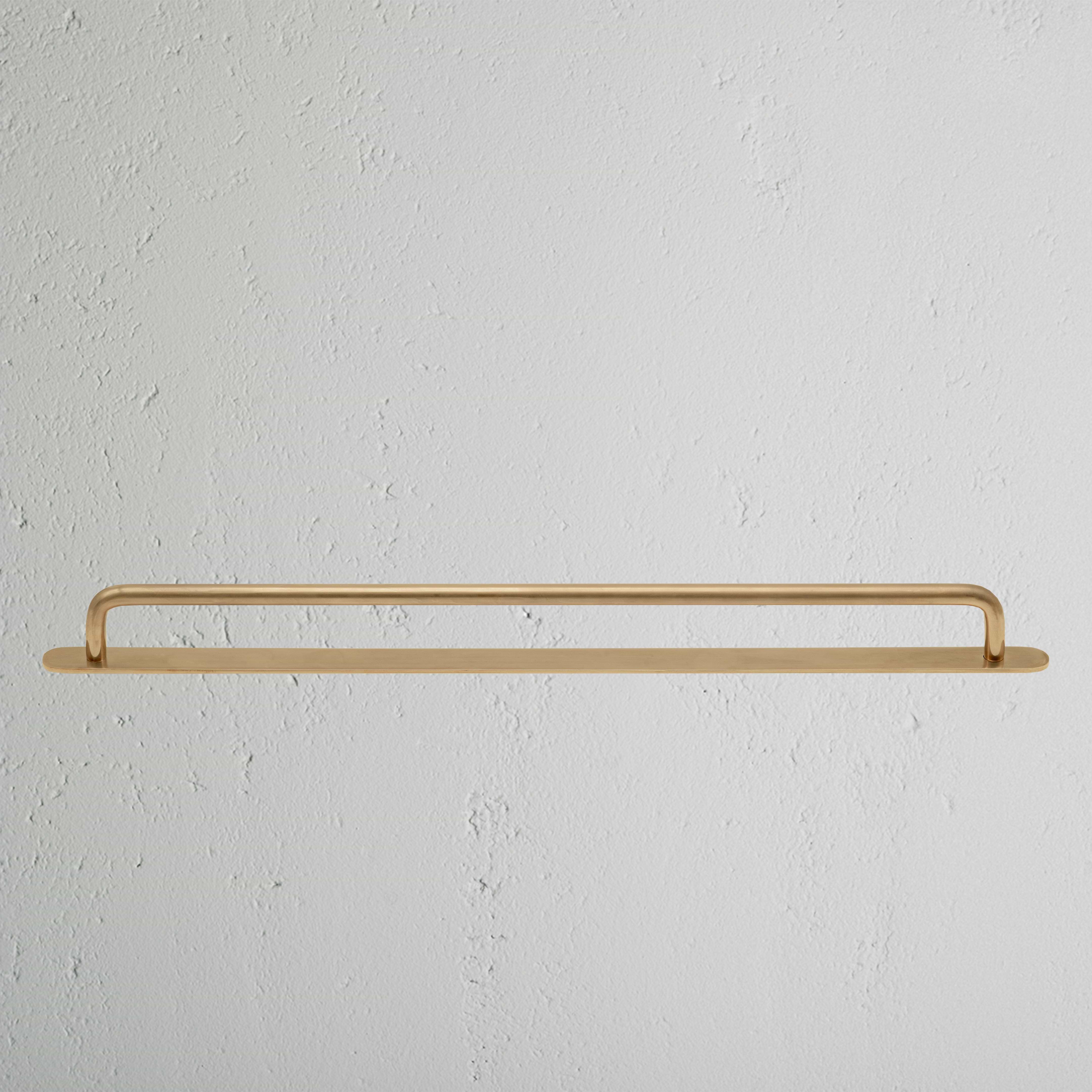 Large antique brass Kilburn furniture handle with rounded ends, mounted on a white textured surface.