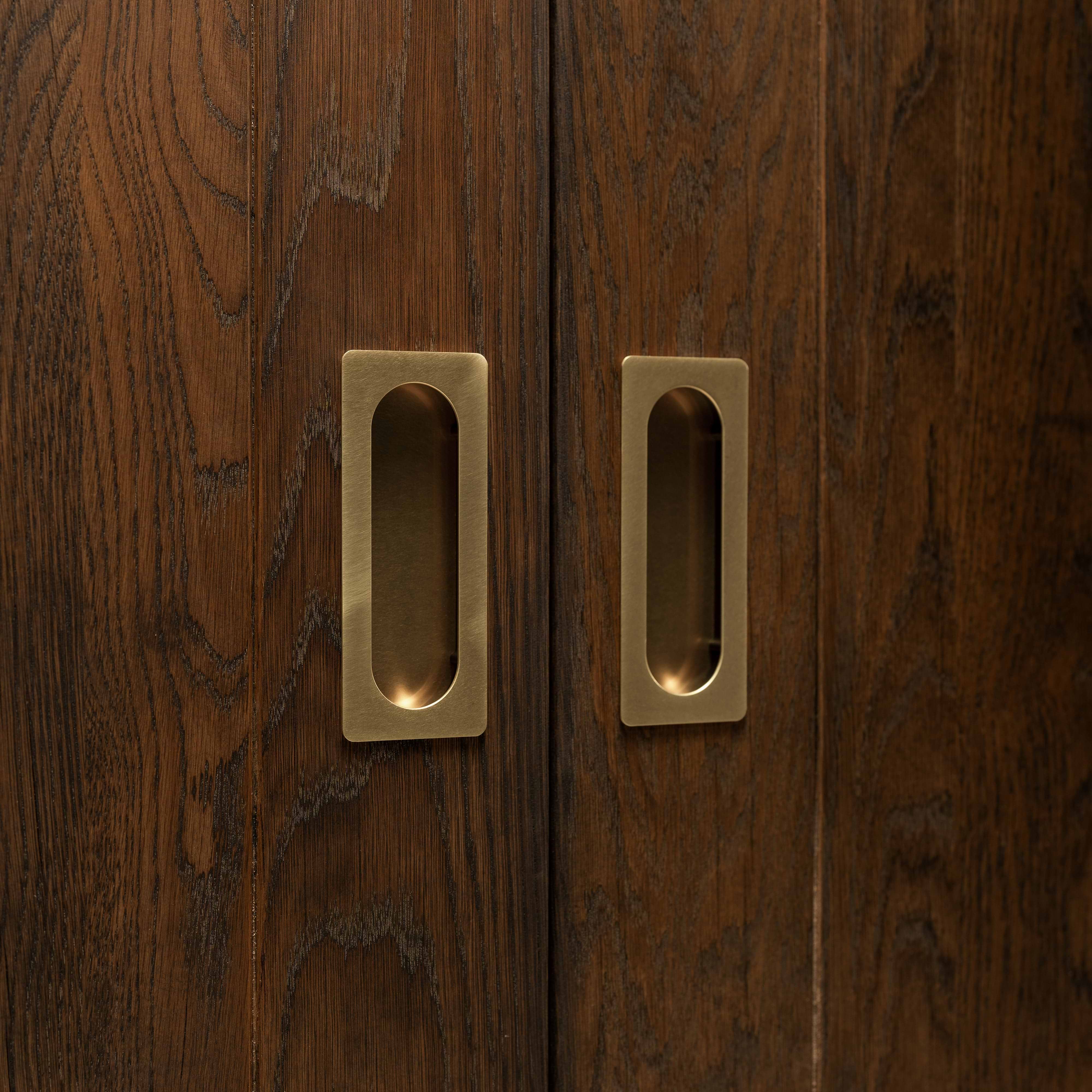 Close-up of Regent Recessed Medium Pull in Antique Brass installed on wooden sliding doors.