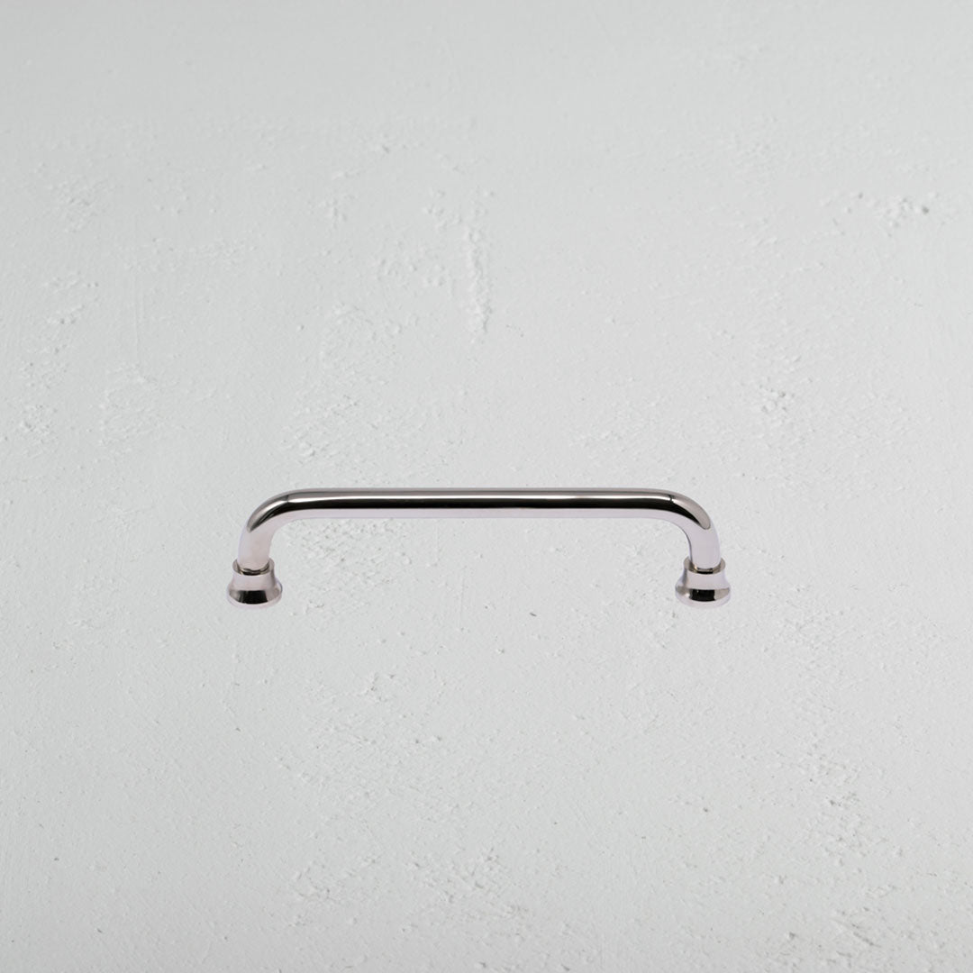 Sycamore Furniture Handle Small in polished nickel, featuring curved edges, mounted on a white surface.