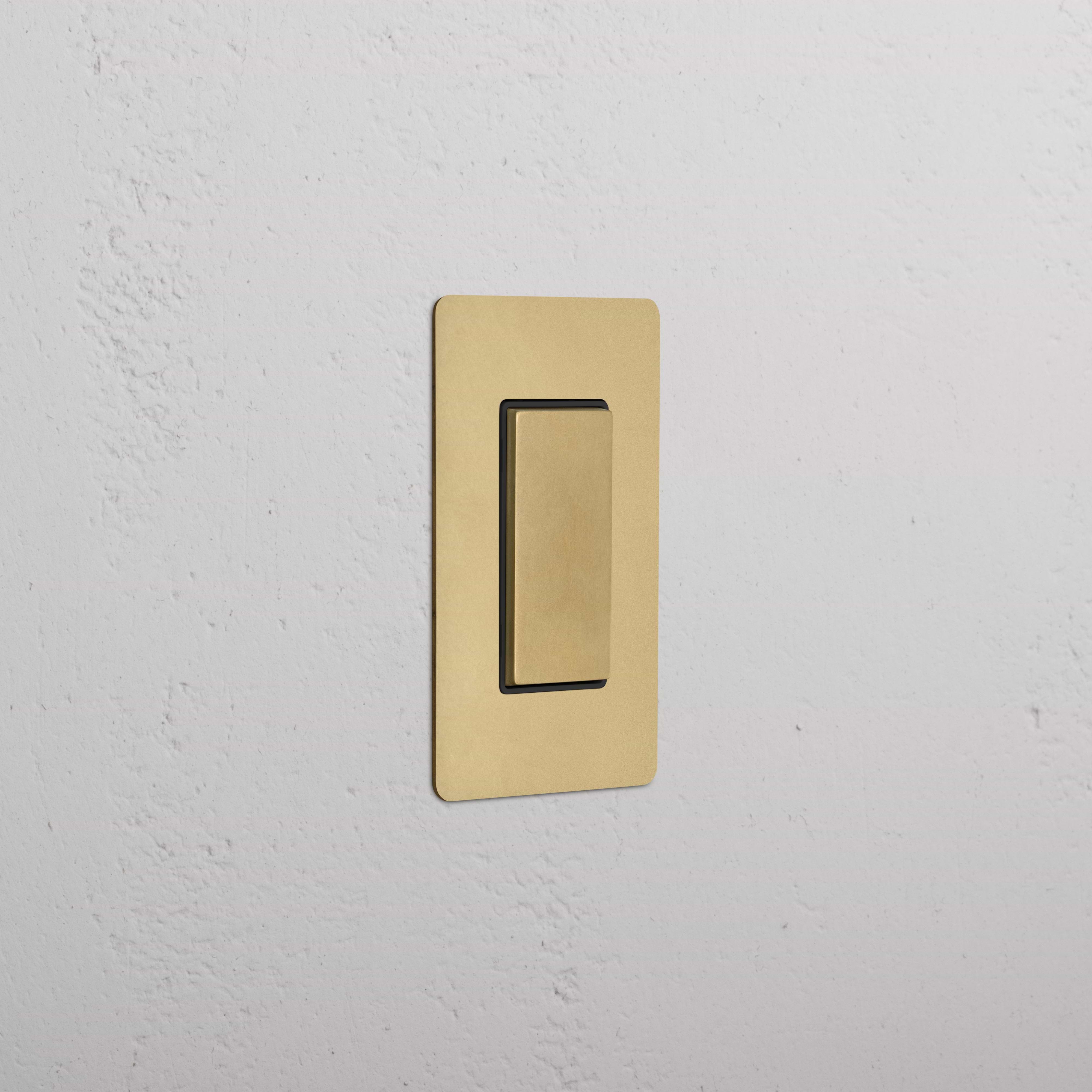 Kew 1G Center Retractive Rocker Switch in Antique Brass Black, rectangular plate, mounted on wall.
