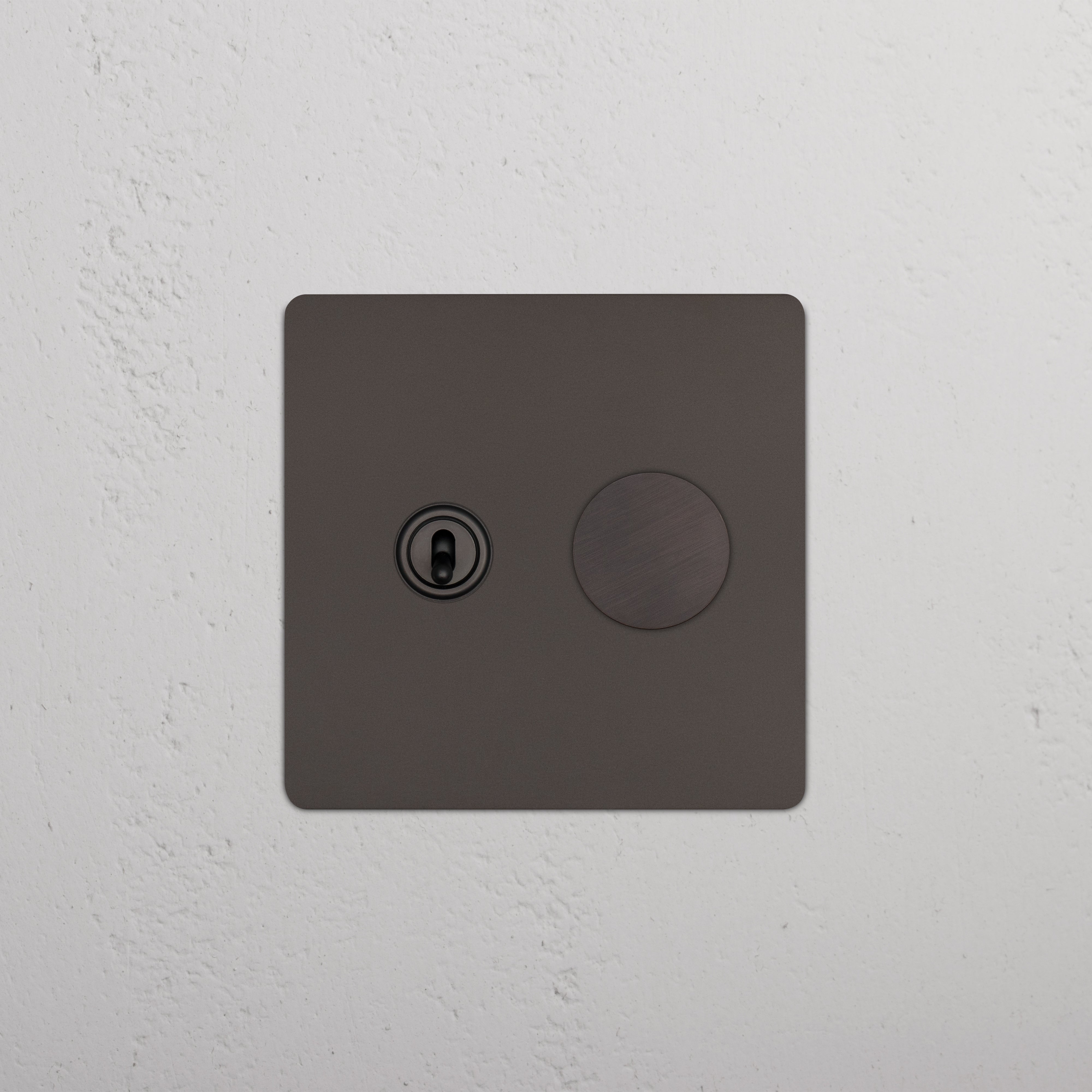 Kew 2G Toggle & Dimmer Switch in bronze, showing one toggle and one dimmer knob on a white wall.